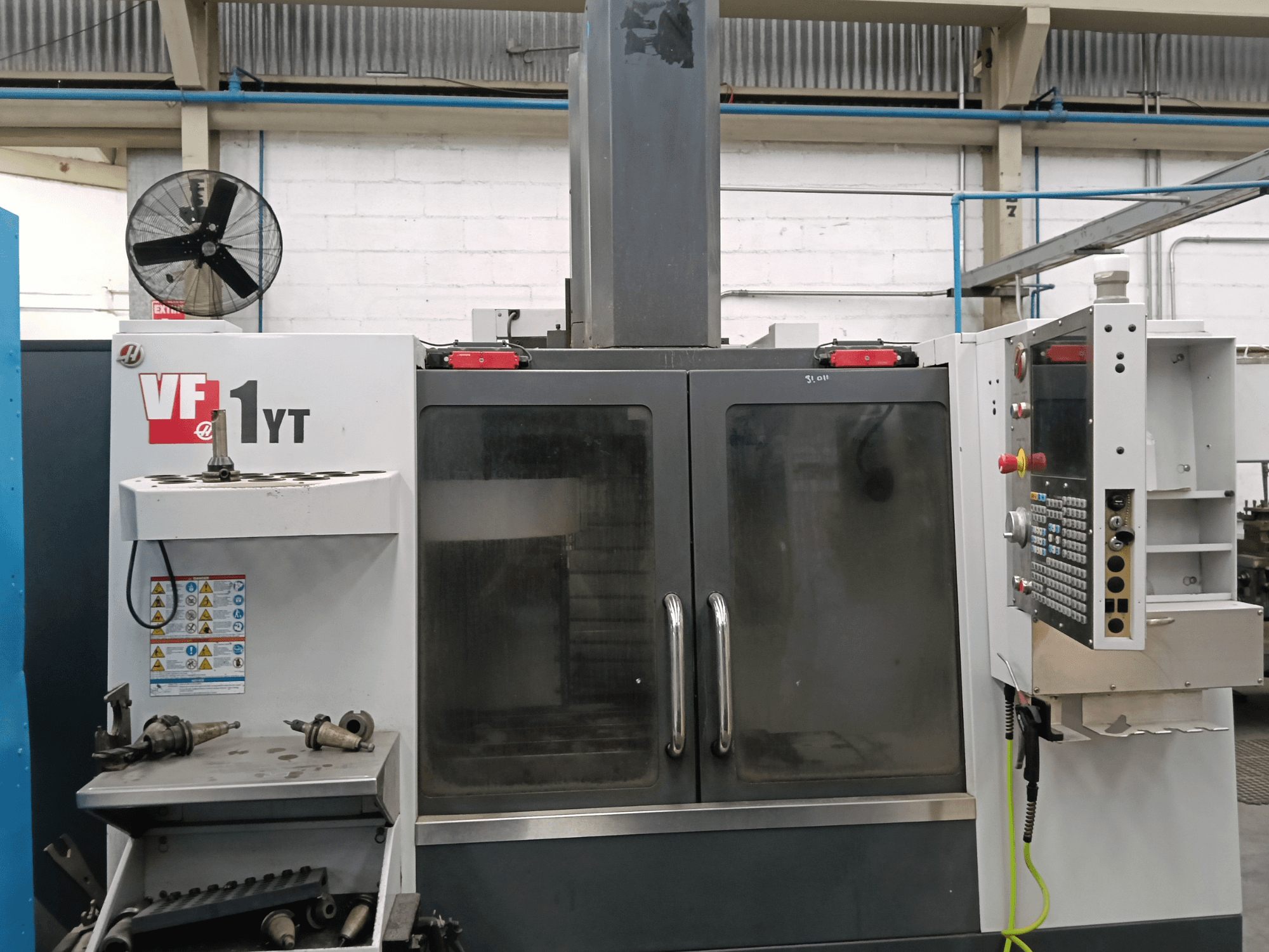 HAAS VF-1YT-1 -pystykoneistuskeskukseen etunäkymä, jossa ohjauspaneeli ja työkalut ovat sivulla.