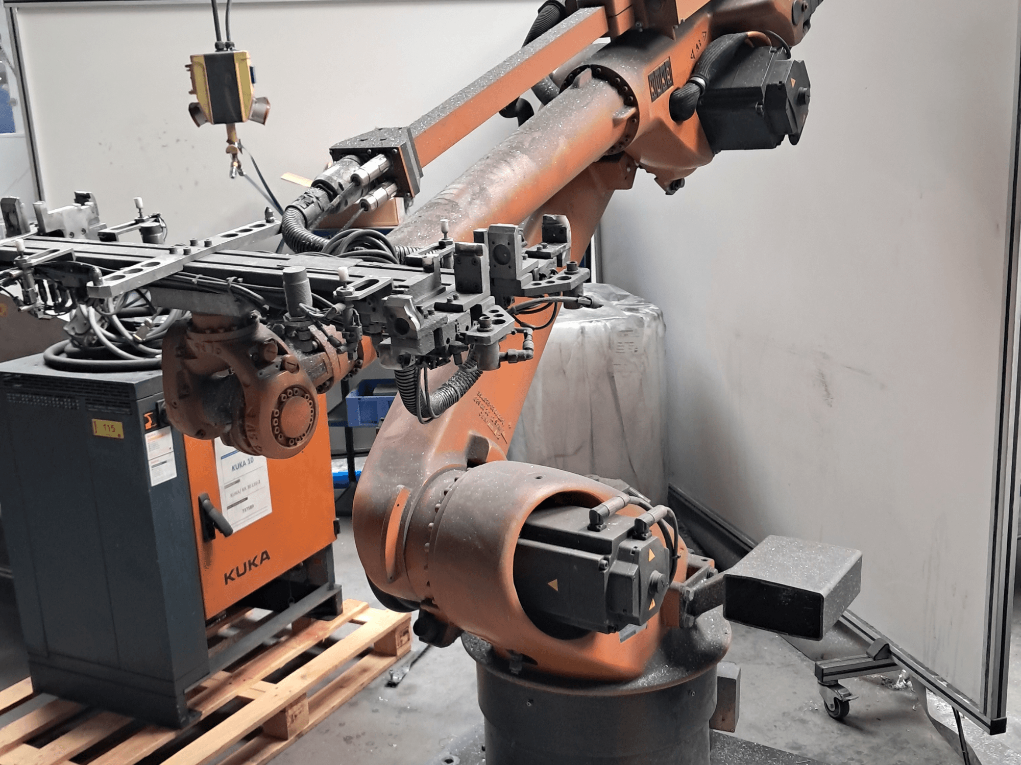 KUKA KR 30L16-2 -robottivarsi sivulta katsottuna, jossa näkyy monimutkainen työkappale ja ohjauskaapelit; kuvassa se on sijoitettu KUKA-ohjauskotelon viereen.