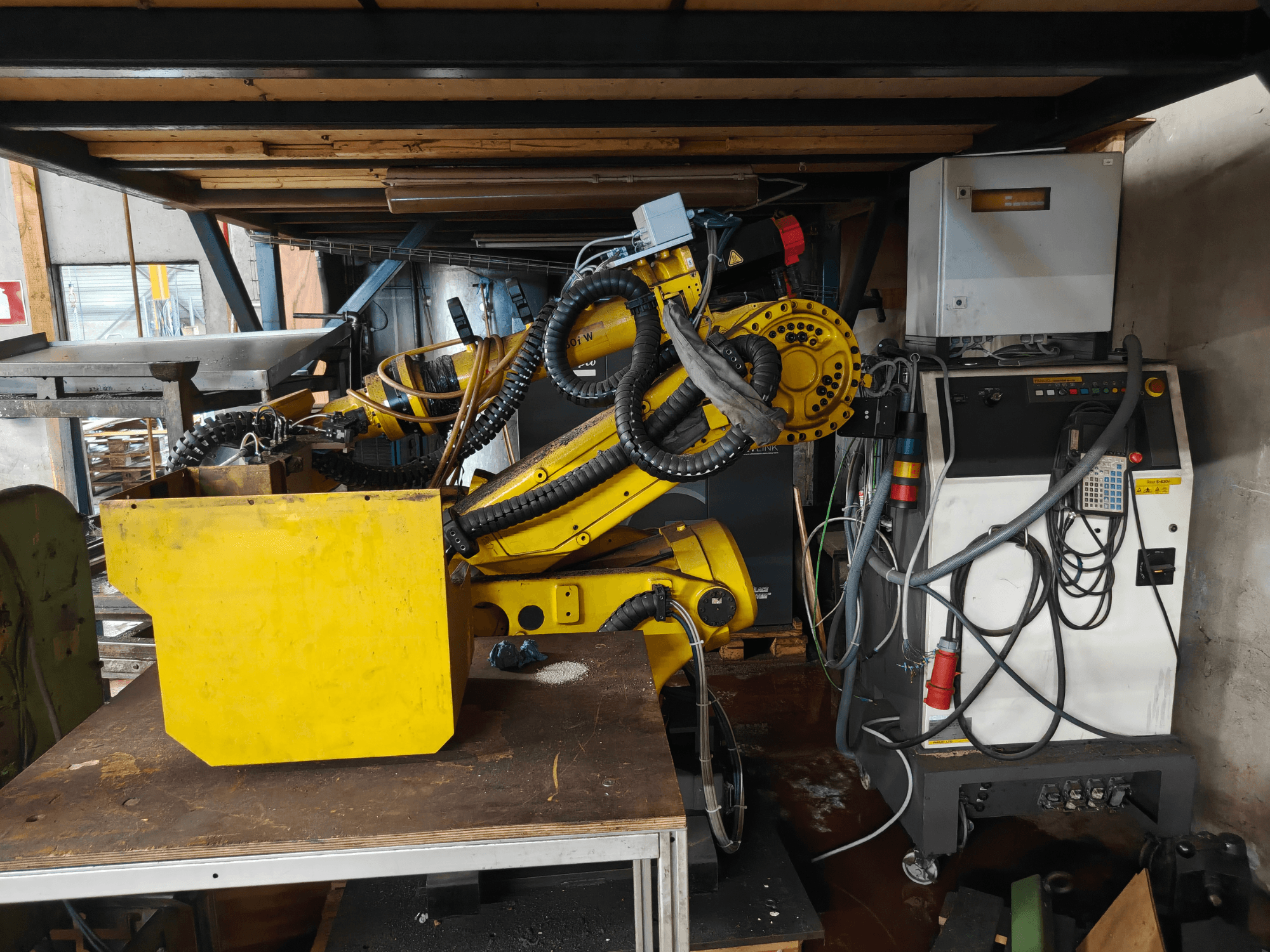 FANUC S-430i W -robotin käsivarren etunäkymä: keltainen, ohjauspaneeli, kaapelit ja keltainen komponentti työpöydällä.