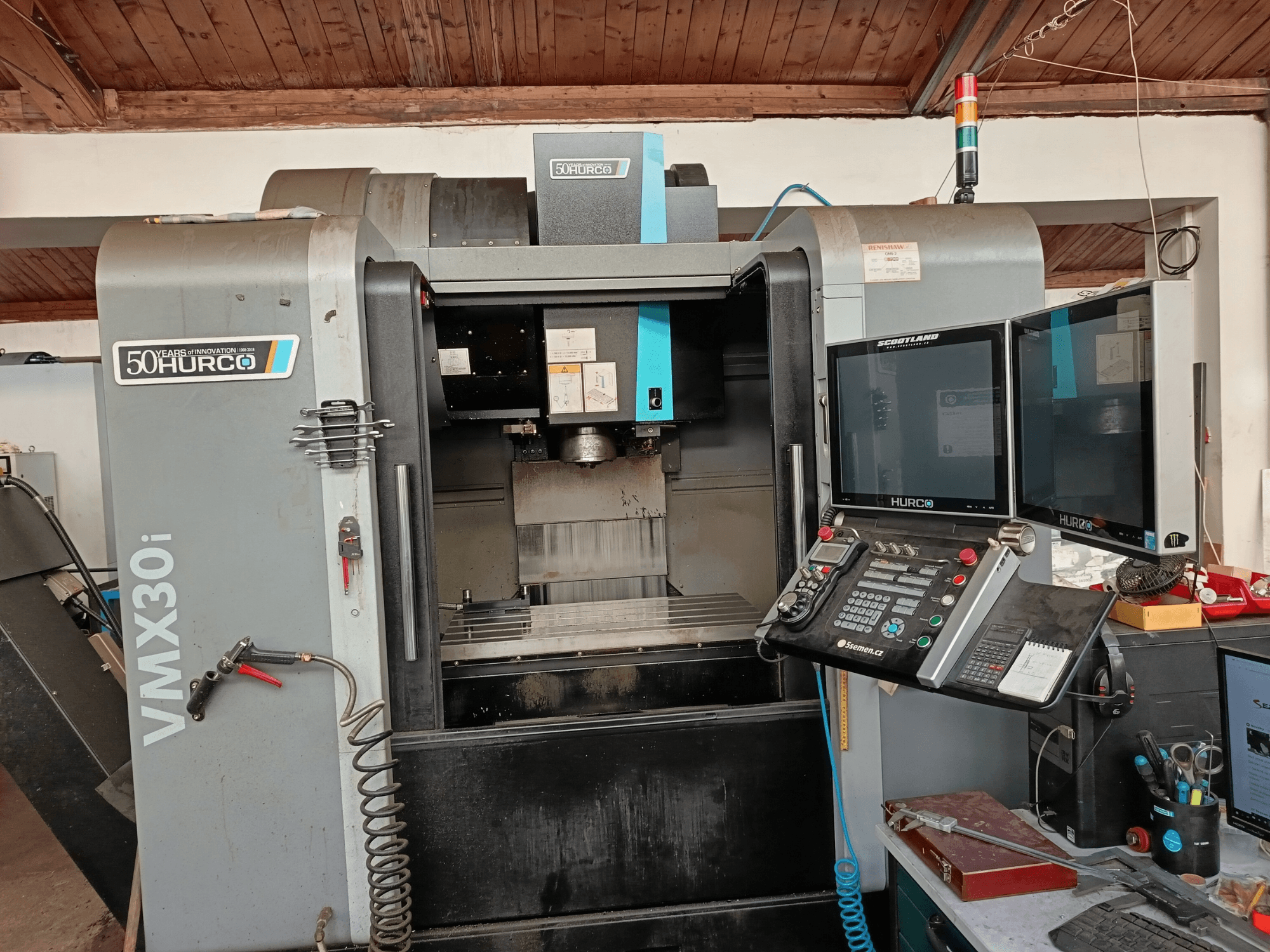 Hurco VMX30i CNC-jyrsinkone etukuvassa, jossa on kaksi näyttöä, ohjauspaneeli ja letku kiinnitettynä.
