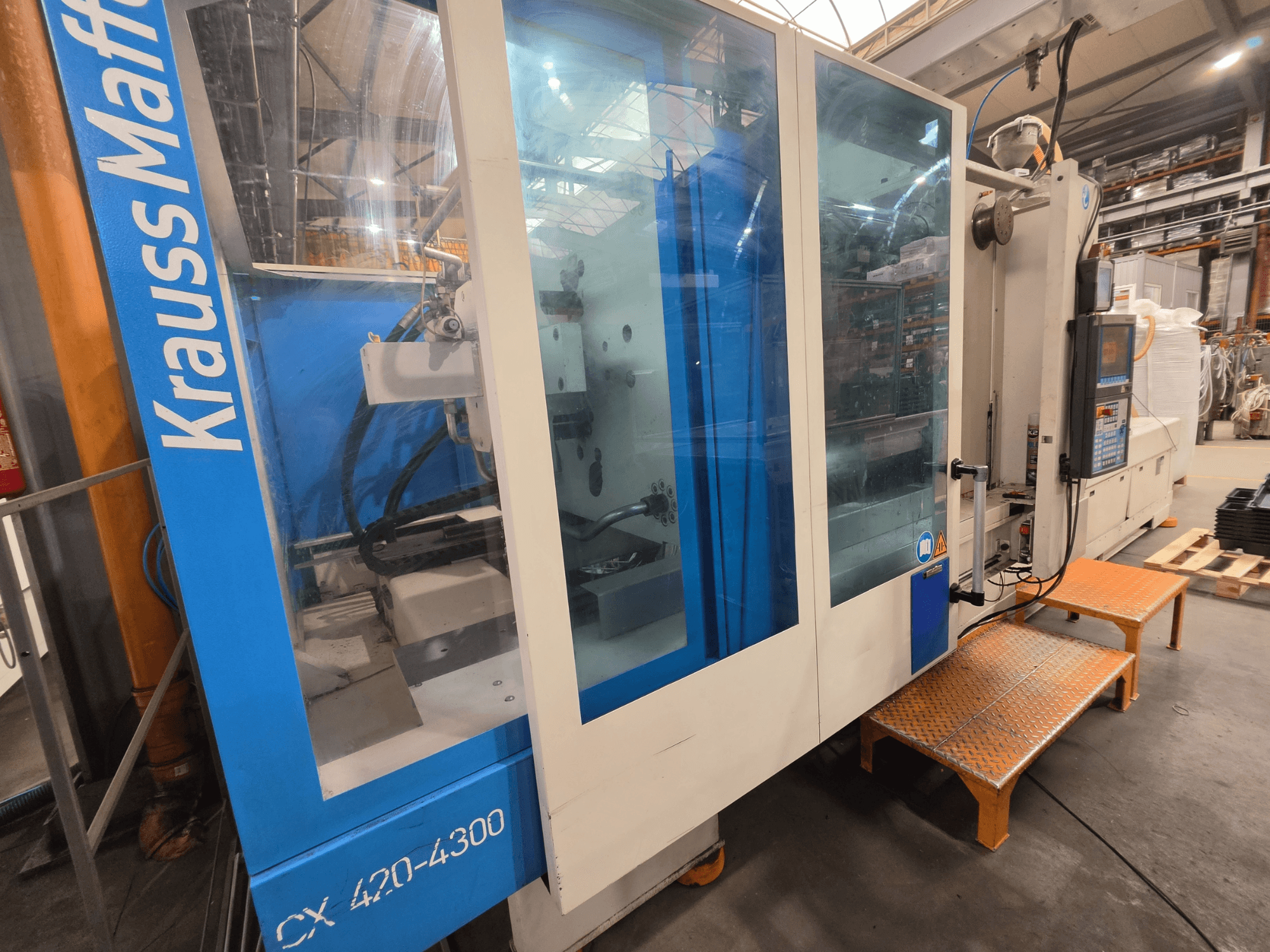 Krauss Maffei CX 420-4300 hydraulinen ruiskuvalukone, sivukuva, jossa näkyy ohjauspaneeli ja läpinäkyvät paneelit.