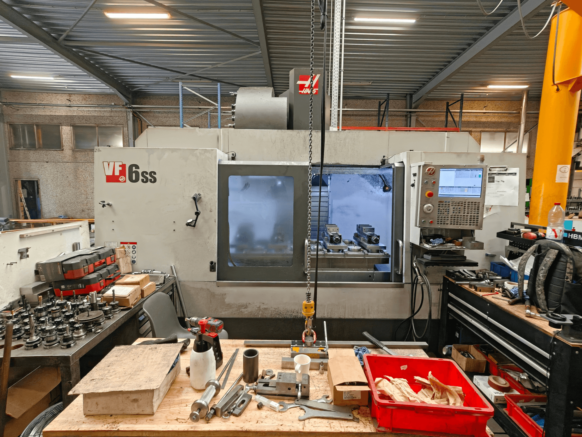 Haas VF-6SS -pystykoneistuskeskus työpajassa; sivukuva, jossa näkyy ohjauspaneeli ja työkaluilla täyttynyt työtila.