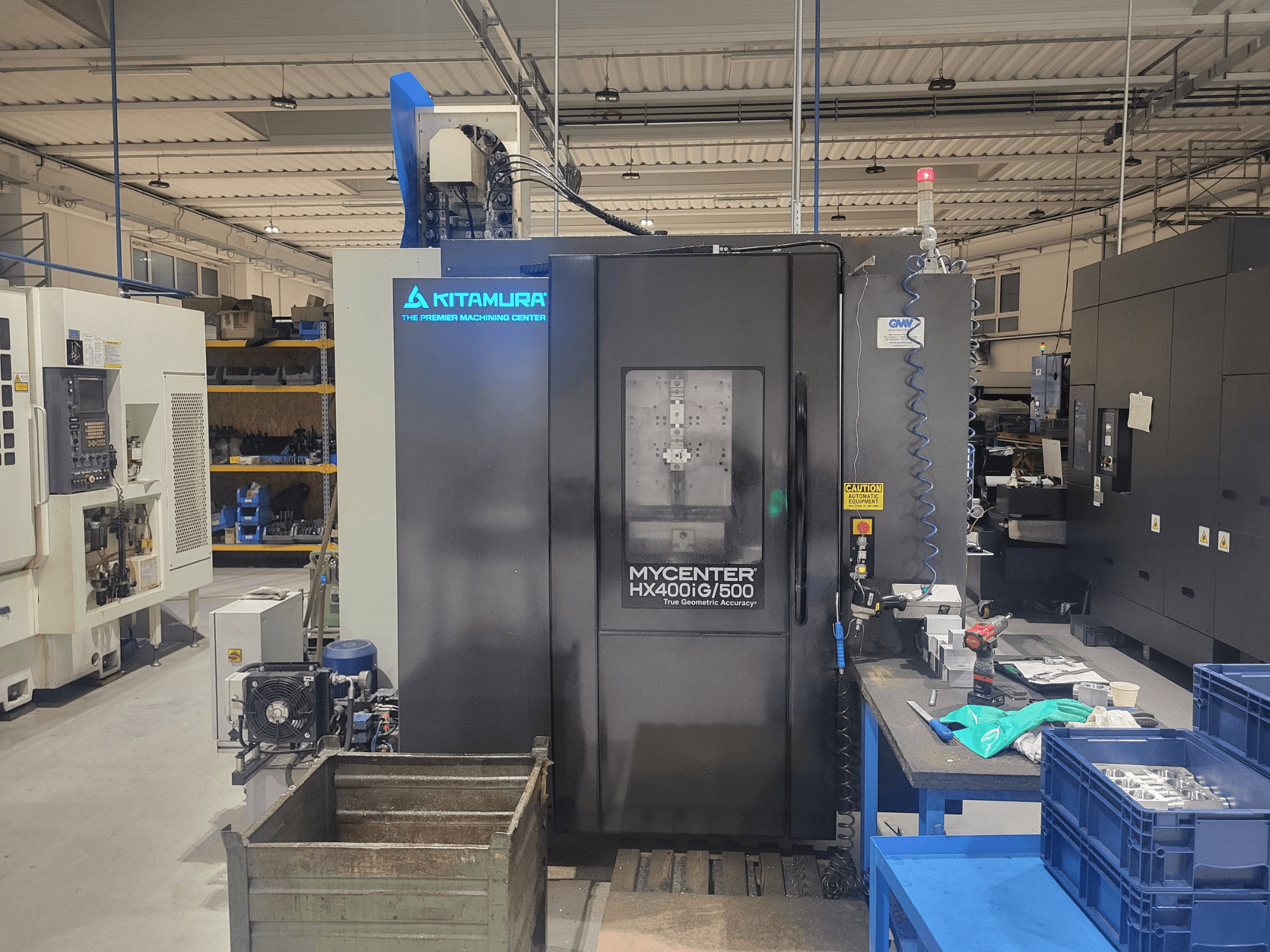 Kitamura Mycenter HX400iG/500 CNC-kone työpajassa, edestä katsottuna, ohjaimet, työkalujen säilytys ja materiaalit lähellä.