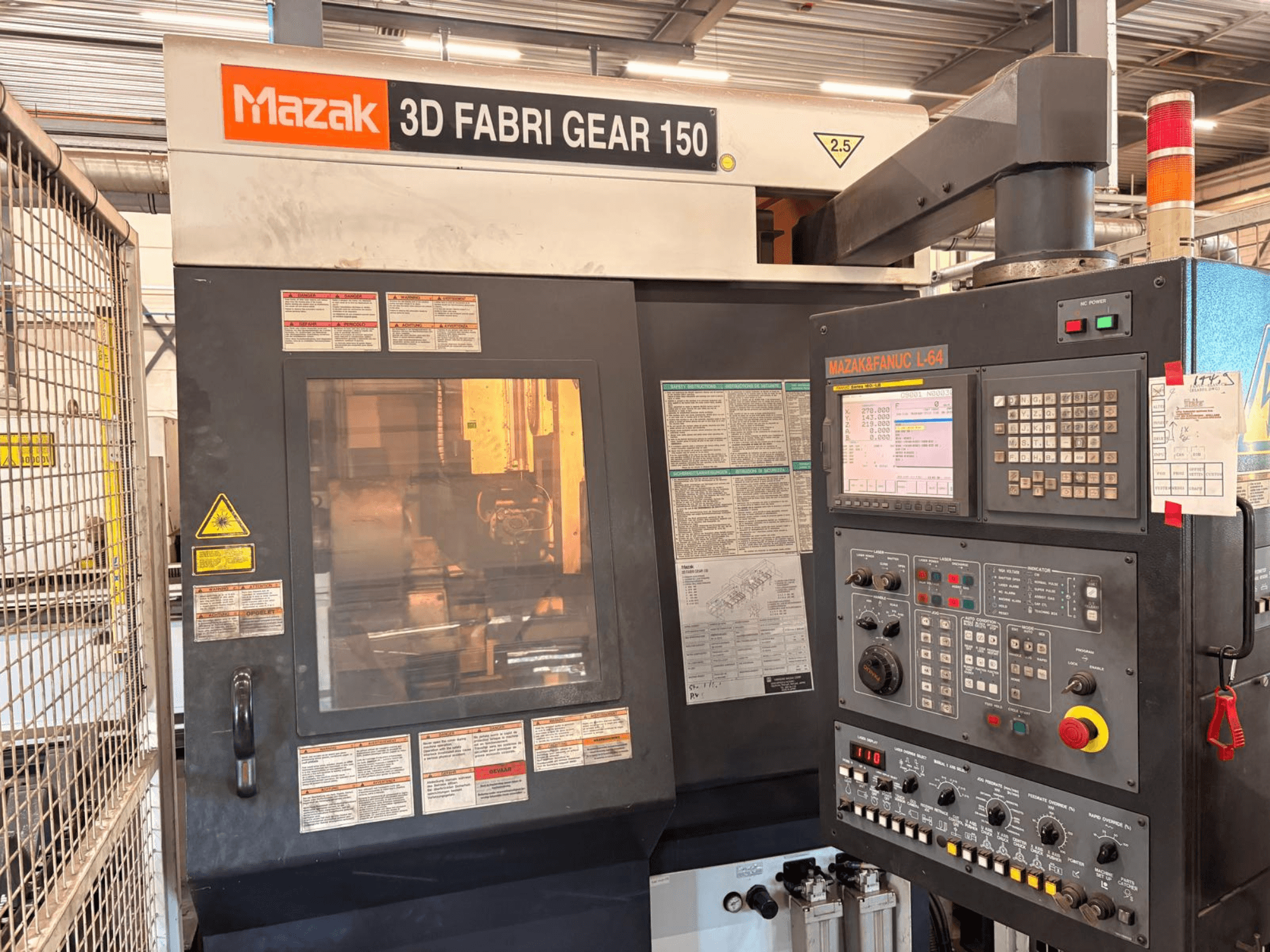 Mazak 3D Fabri Gear 150 -putkenleikkauskone, etunäkymä, jossa näkyvät ohjauspaneeli, turvallisuusmerkinnät ja käyttöliittymä.