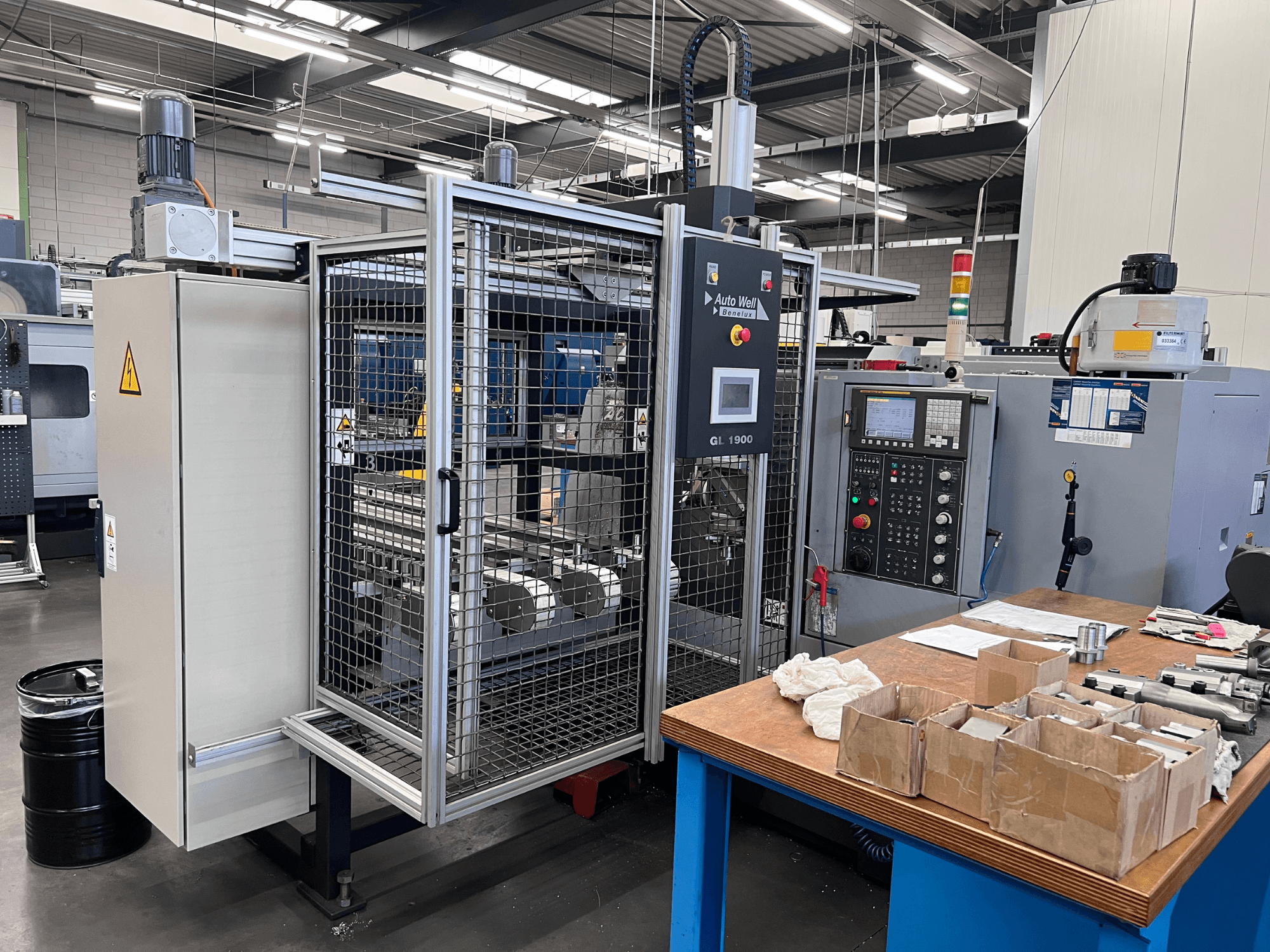 Etukuva Auto Weld GL 1900 -koneesta, jossa on ohjauspaneeli, suojakotelo ja ympäröivät työkalut työpöydällä.