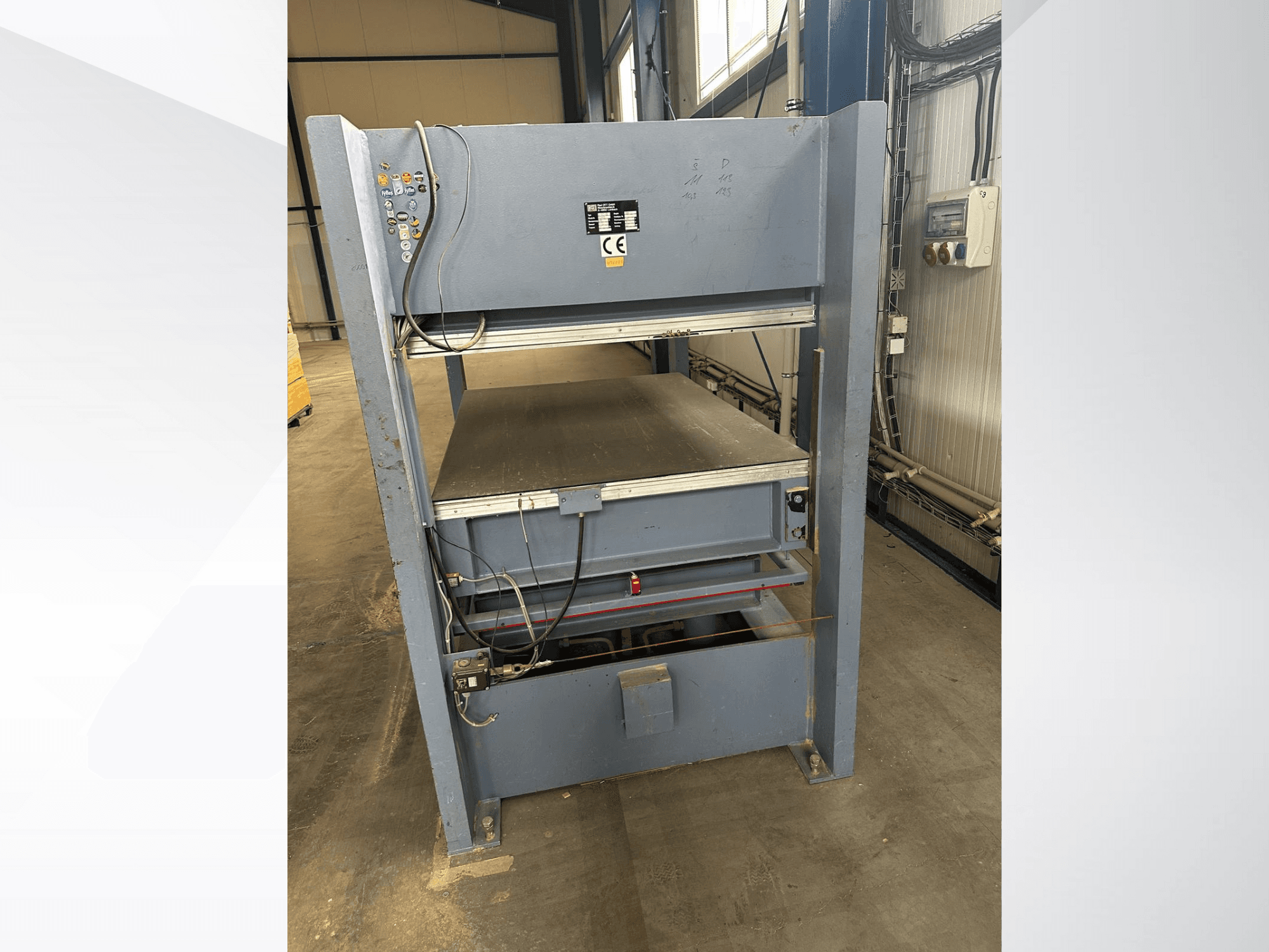 Harmaa teollisuuskone, jossa on ohjauspaneeli edestä katsottuna; sisältää säädettävät alustat ja turvamerkinnät.