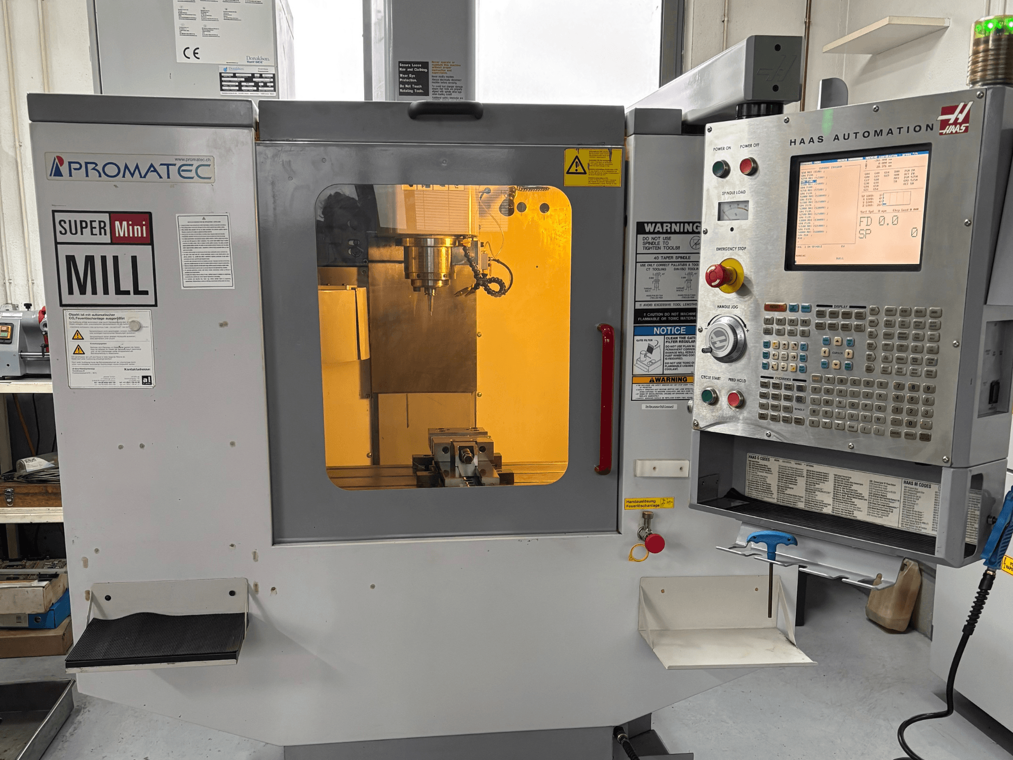 Promatec Super Mini Mill -jyrsin edestä katsottuna, varustettu Haas Automation -ohjauspaneelilla ja näkyvällä leikkuutyökalulla sisällä.