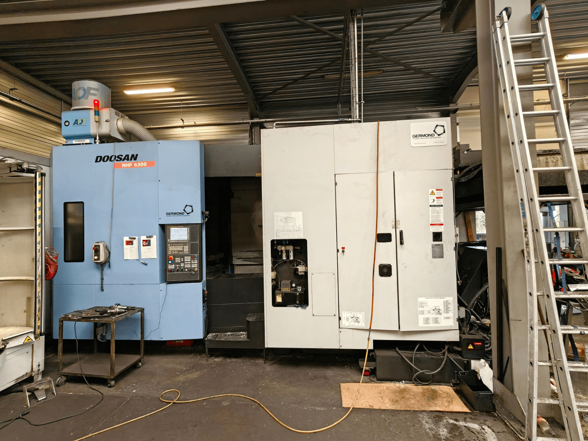 DOOSAN NHP6300 -vaakakoneistuskeskus edestä katsottuna; kuvassa näkyy ohjauspaneeli ja sen vieressä olevat koneet työpajaympäristössä.