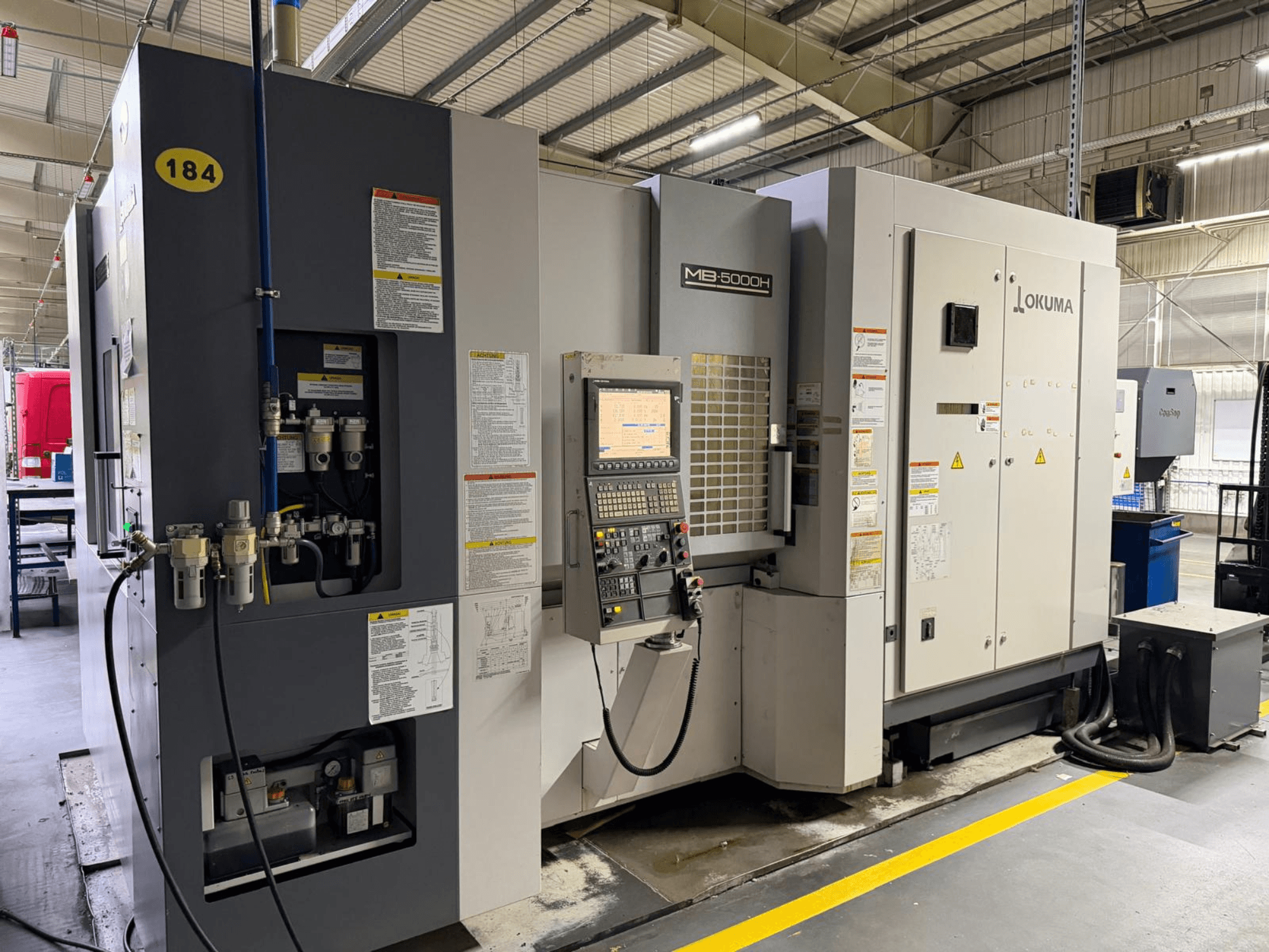Okuma MB 5000H -vaakakoneistuskeskuksen etukuva, jossa on hallintalaitteet, merkinnät ja hydrauliset liitännät.