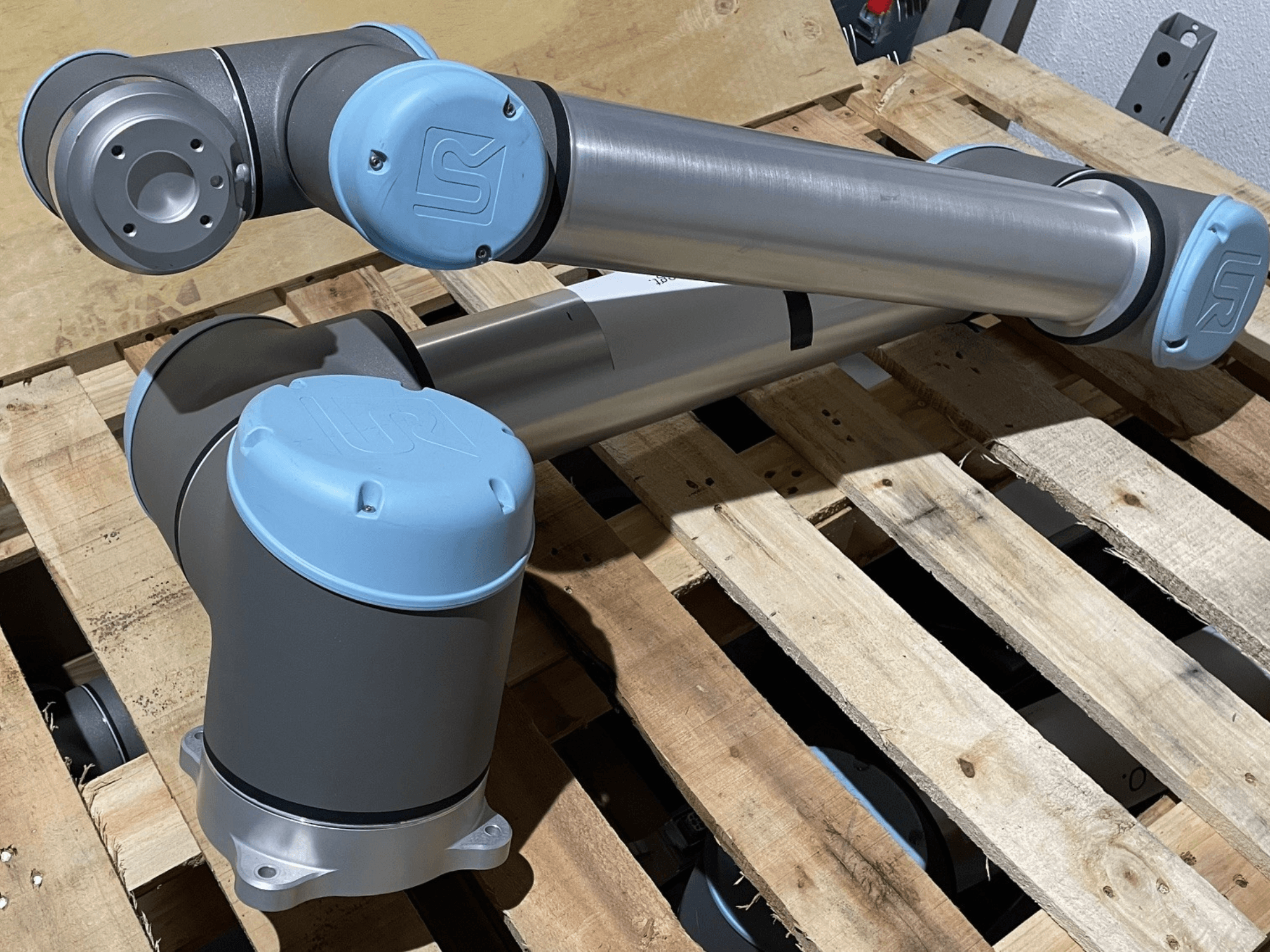 Hopeinen robottikäsi, jossa on siniset päätykappaleet, etukuva, jossa näkyvät nivelet ja mekaaniset yksityiskohdat, lepää puulavalla.