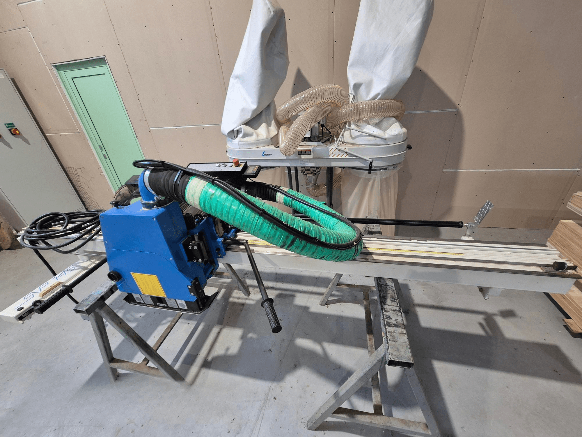 Sininen SVP-175-vaakalevysaha, jossa on vihreä pölyletku ja tuki, sivulta katsottuna työpajassa.