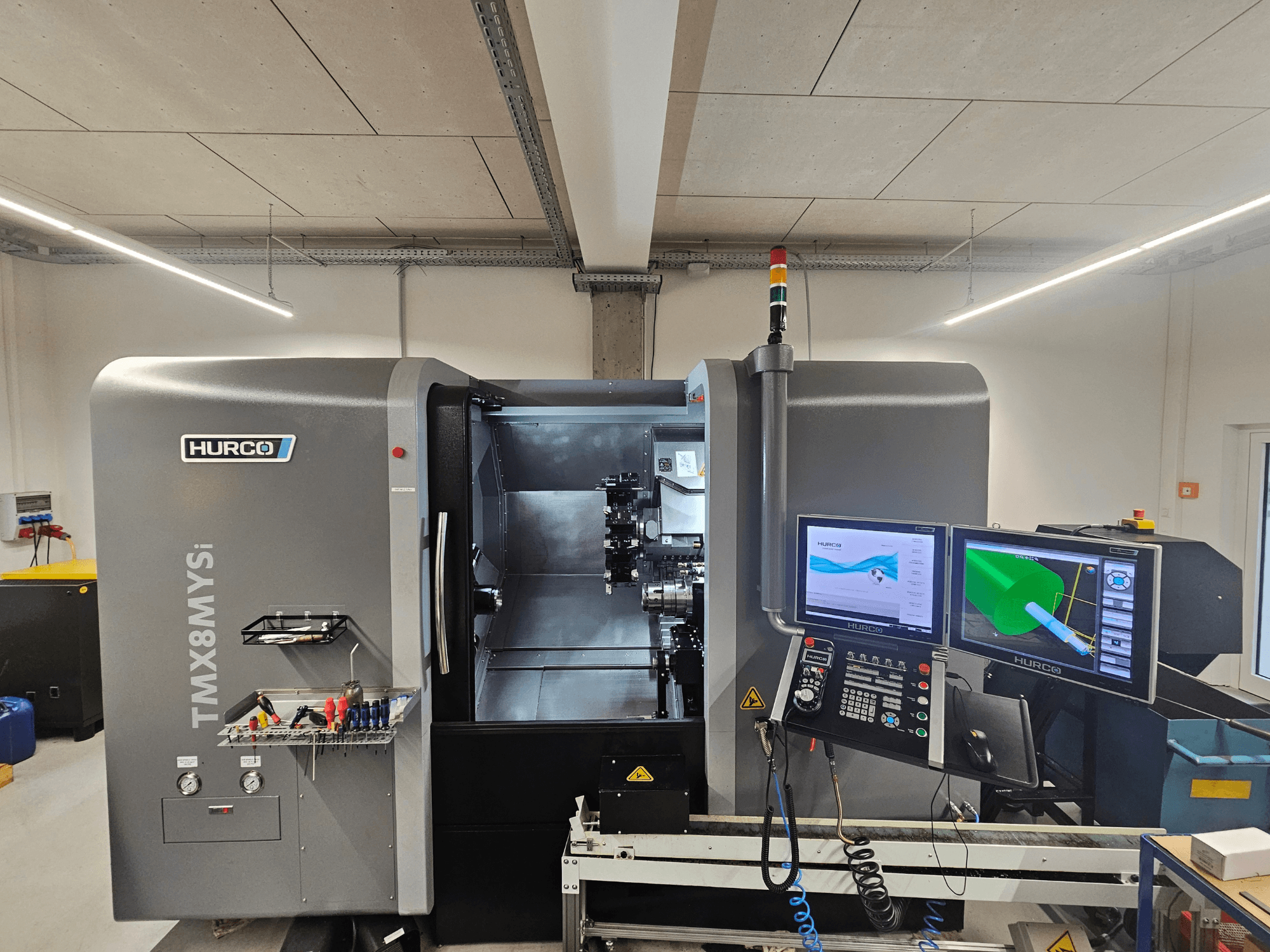 Hurco TMX 8 MYSi -kääntökeskus työpajassa, jossa on kaksi näyttöä, ohjauspaneeli ja työkalut sivulla.