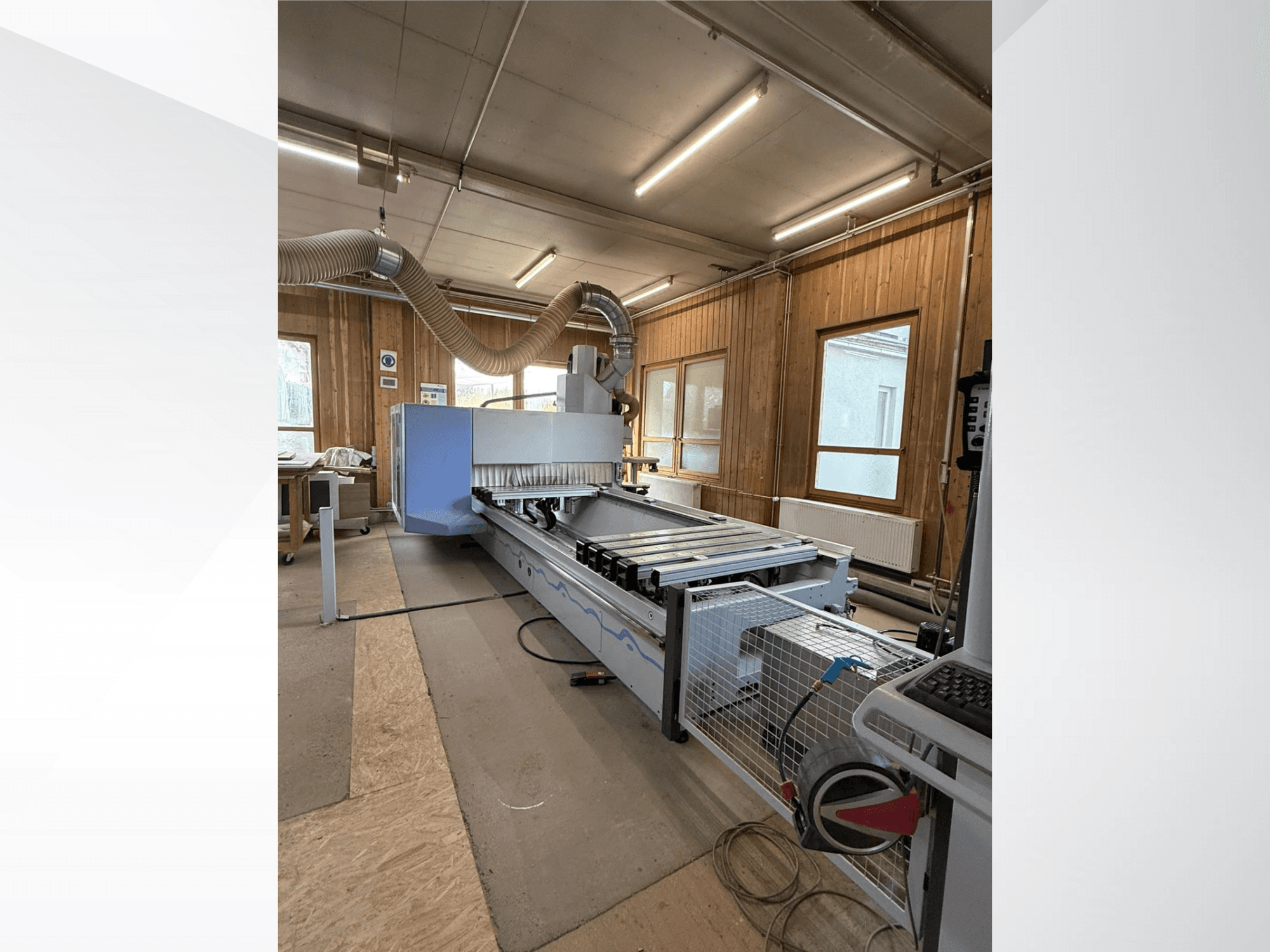 CNC-jyrsinkone työpajassa, sivukuva, jossa on suuri sininen runko, kiinnitetty hihnakuljetin ja näkyvä ohjauspaneeli.