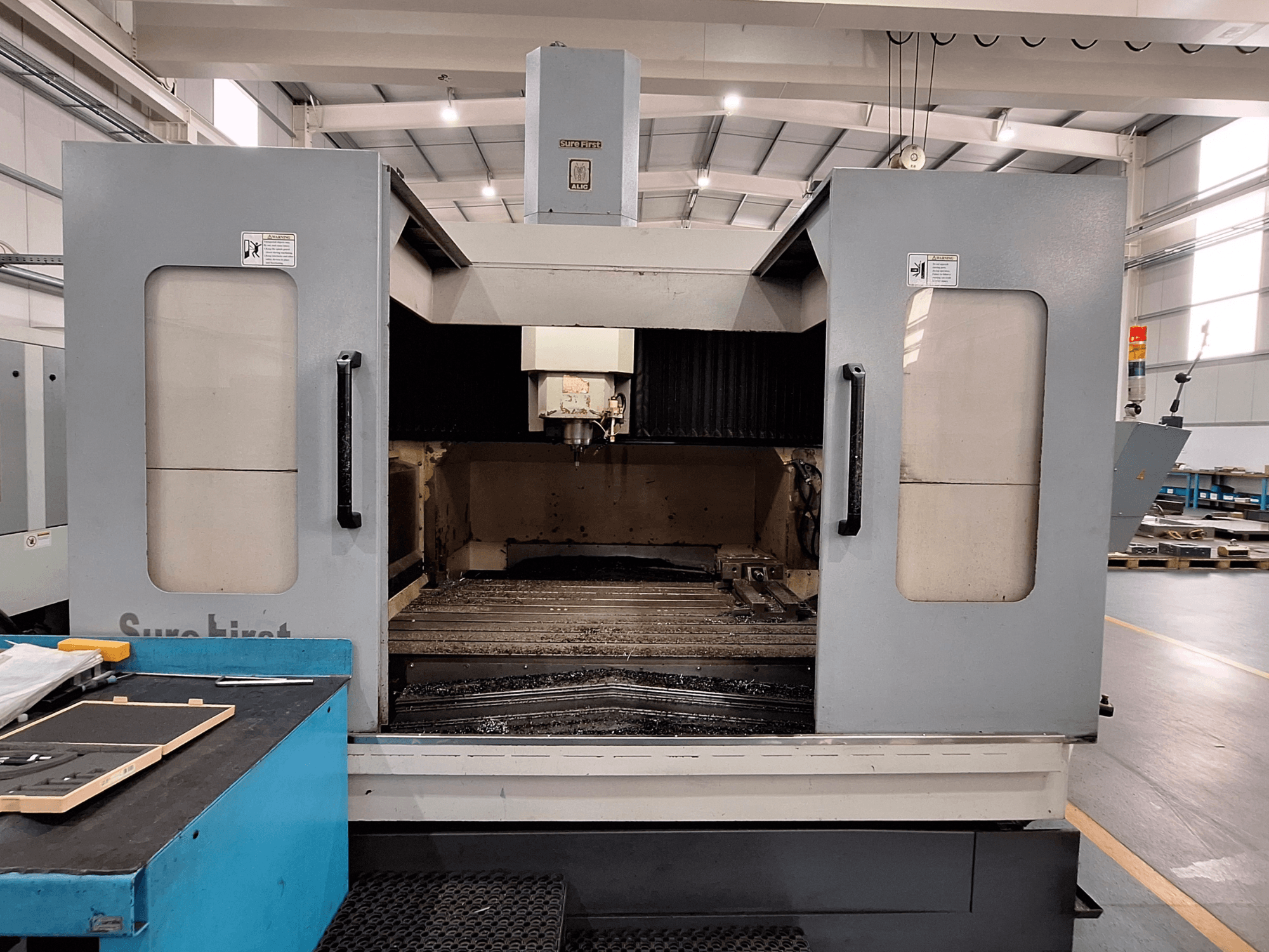 Pystytyöstökeskus Sure First QM-1836, etukuva, jossa näkyy työkalupää ja tyhjä työalue, moderni teollisuusympäristö.