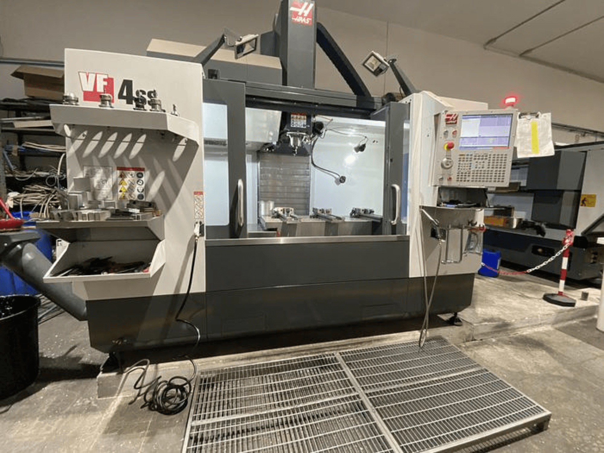Haas VF-4SS CNC-jyrsinkone, etukuva, jossa on työkalujen säilytys, ohjauspaneeli ja näkyvä työalue työpajassa.