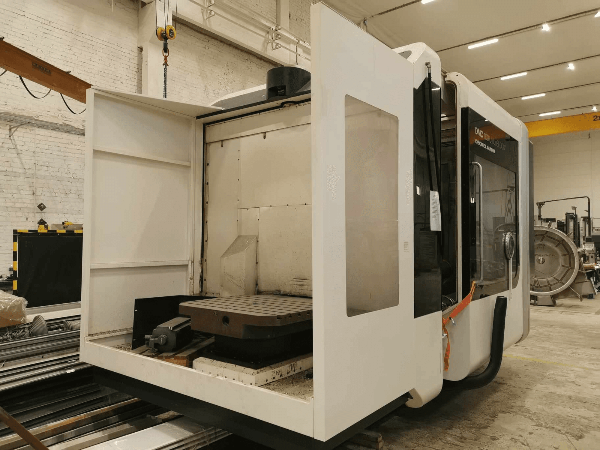 DMC 100U lineaarinen CNC-kone, sivukuva avoimesta luukusta, jossa näkyy työpöytä ja sisäiset komponentit.