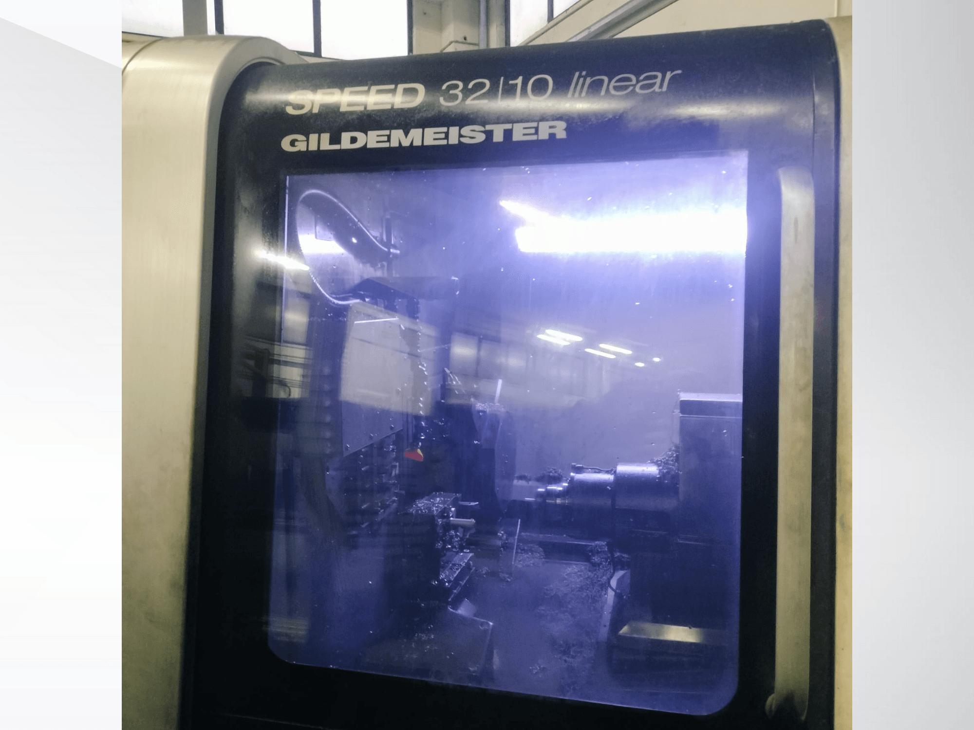 Gildemeister SPEED 3210 lineaarisen CNC-koneen etukuva, jossa näkyvät sisäiset komponentit ja nestemäinen jäähdytysneste käytössä.