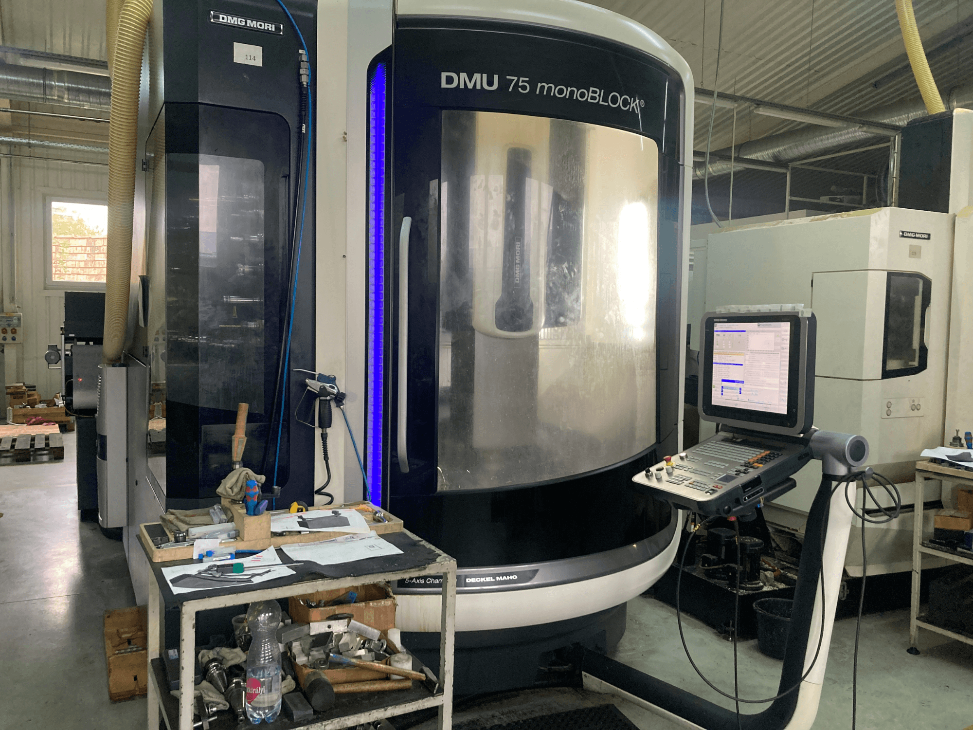 DMG MORI DMU 75 monoBLOCK® CNC-kone, etukuva, jossa on ohjauspaneeli, työkaluja ja työtila materiaaleineen.