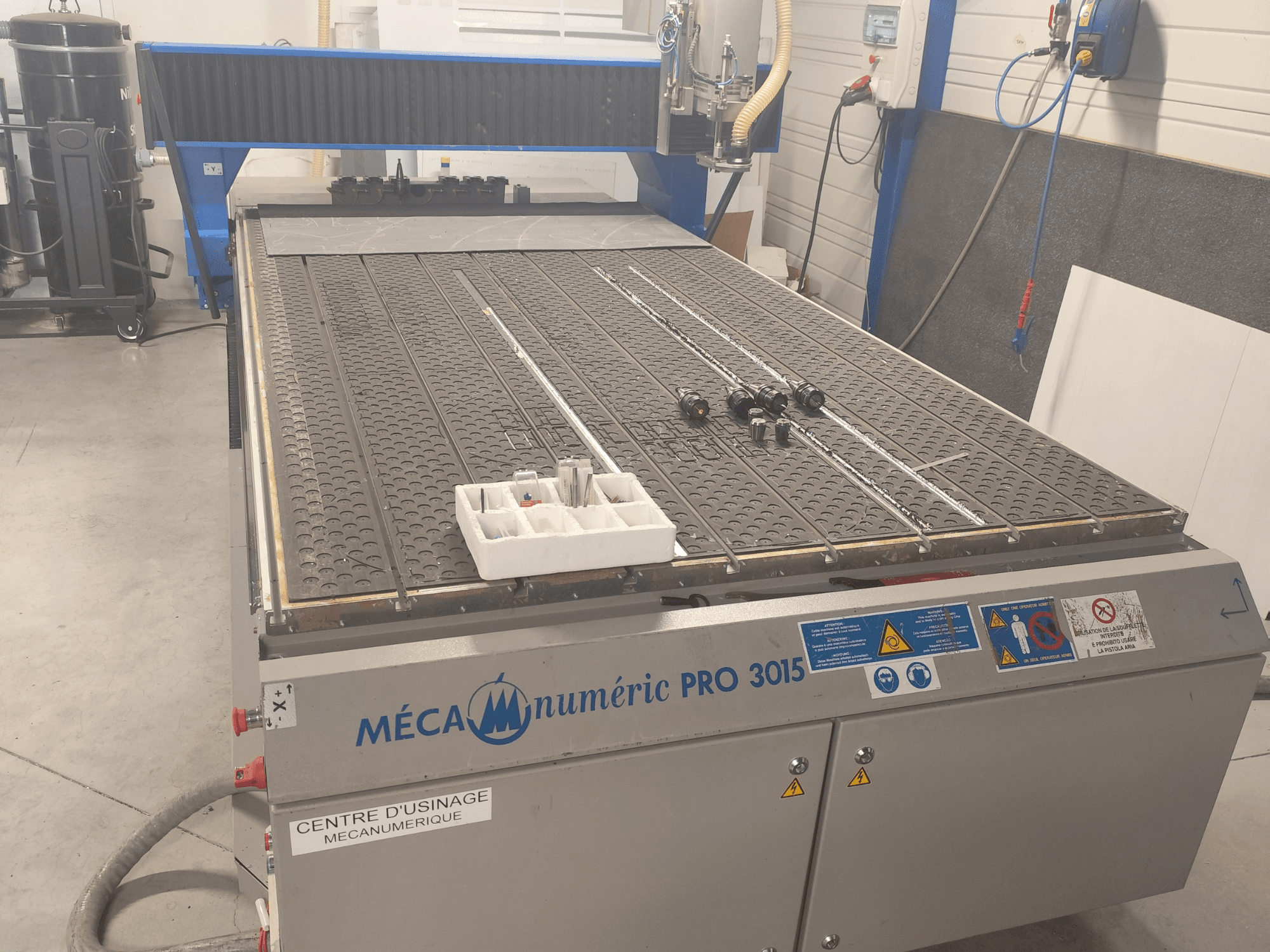 CNC-jyrsin MECANUMERIC Pro 3015 edestä katsottuna; kuvassa näkyy yksityiskohtaisesti leikkuualusta, ohjauspaneeli ja pöydällä olevat lisävarusteet.