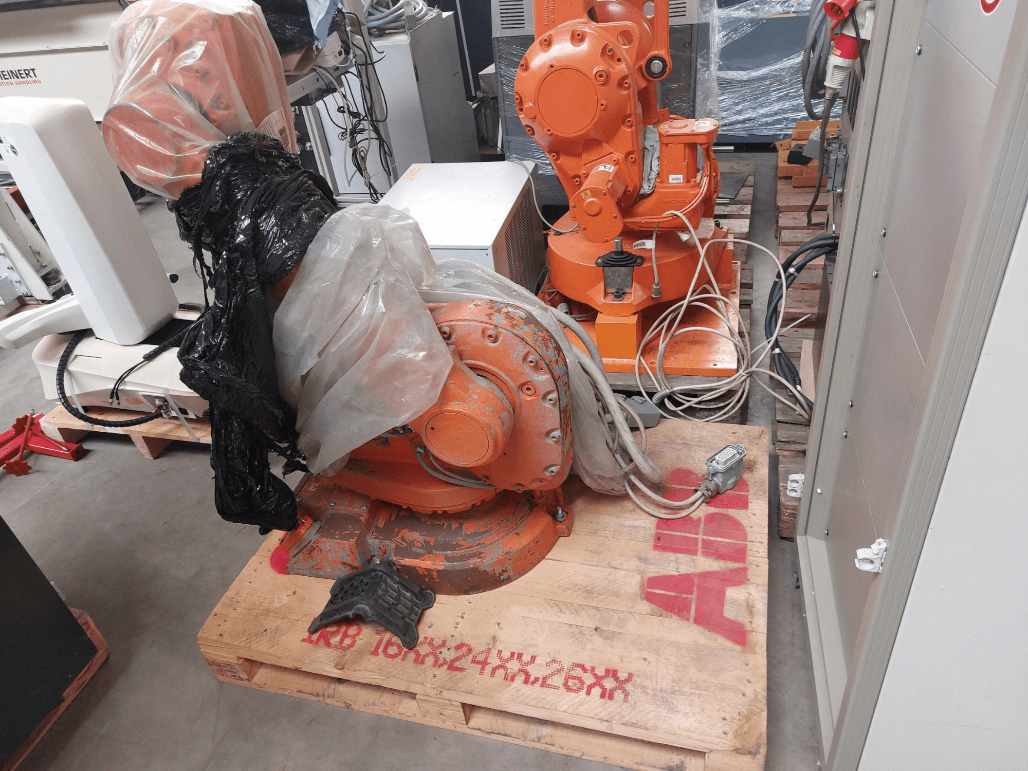 ABB IRB 1600 M2004 -robottivarsi osittain muovin peittämä, edestä katsottuna, kaapelit ja lisäkoneet lähellä.