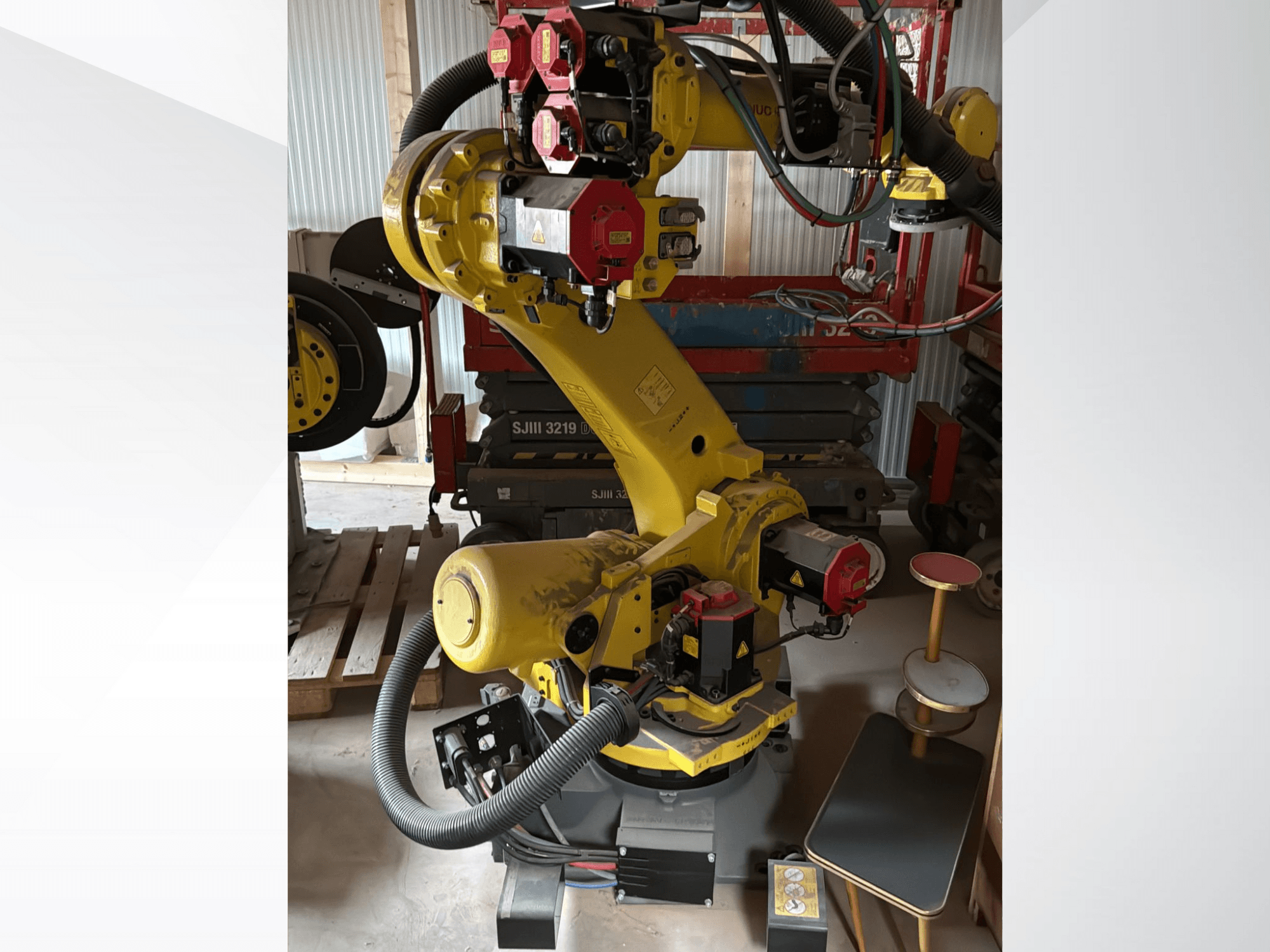 Keltainen teollisuusrobottikäsi, jossa on punaiset ohjaimet, etukuva; siinä on useita niveliä ja letkuja, asetettu työmaalle.
