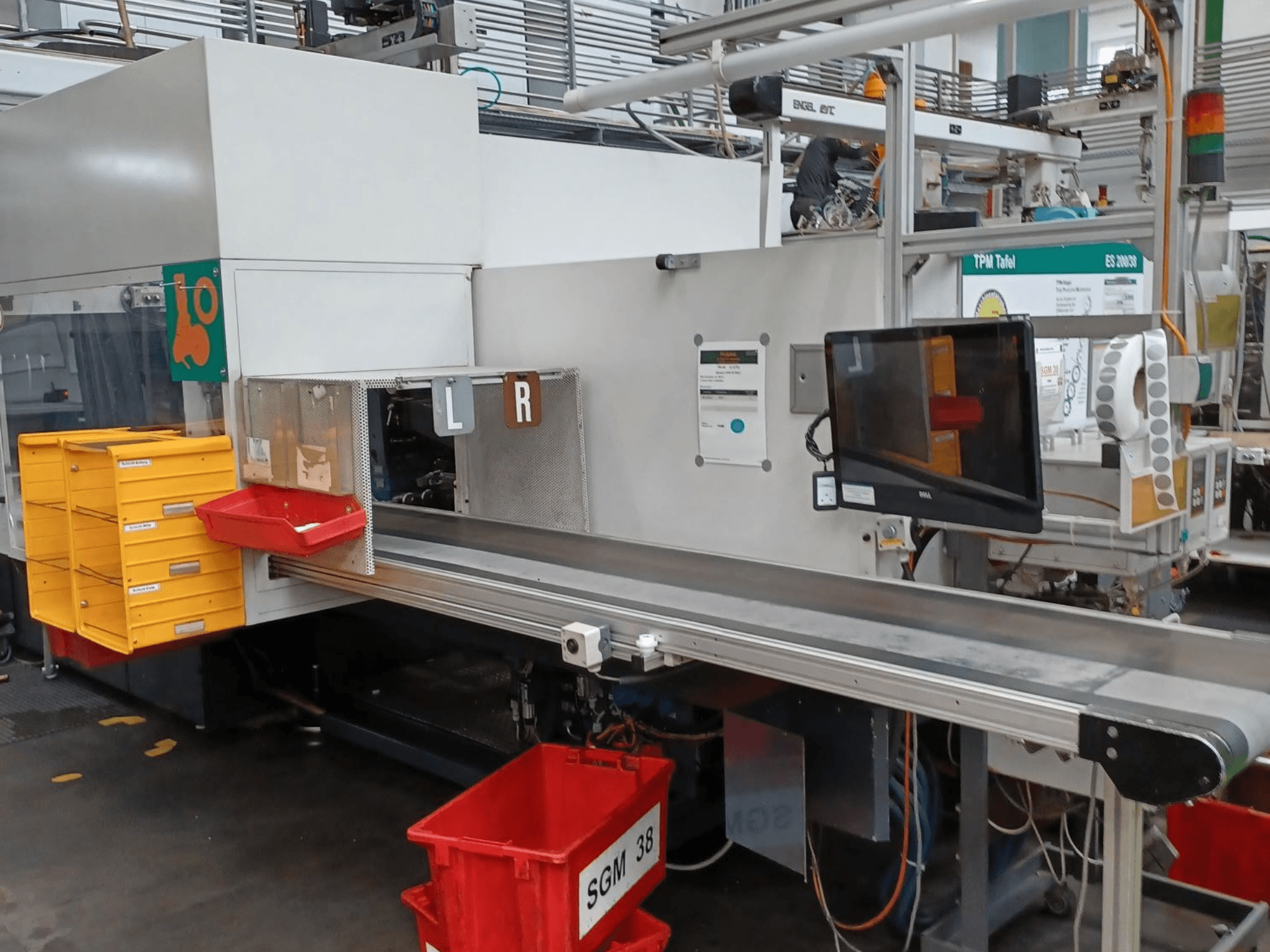 Teollinen lajittelukone keltaisilla ja punaisilla säiliöillä, sivukuva, jossa on valvontamonitori ja merkittyjä osastoja lajittelua varten.