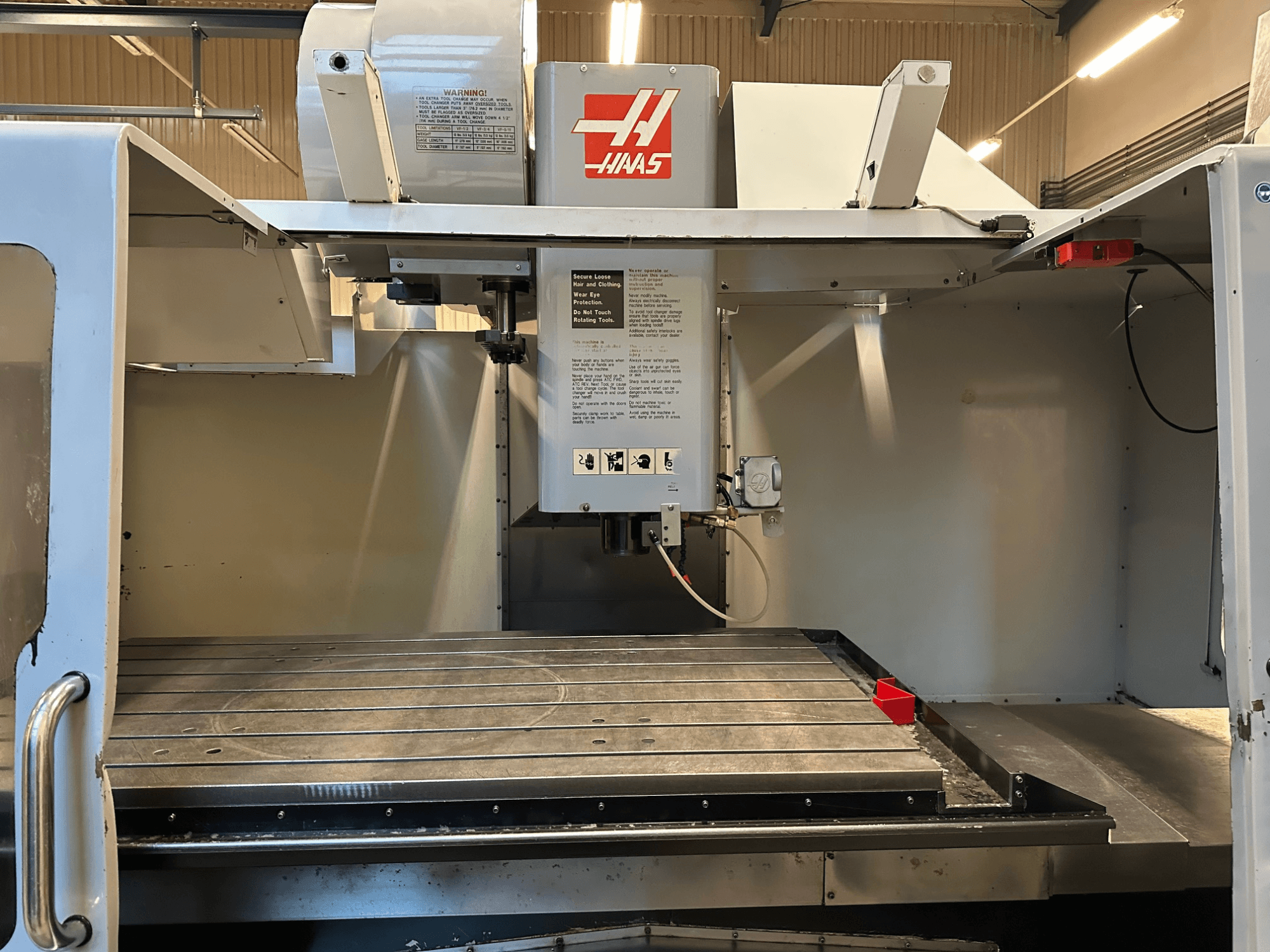 Haas CNC-jyrsin, malli VF-2, etukuva, jossa näkyvät hallintalaitteet, metallinen työpöytä ja paneelissa oleva turvatarra.