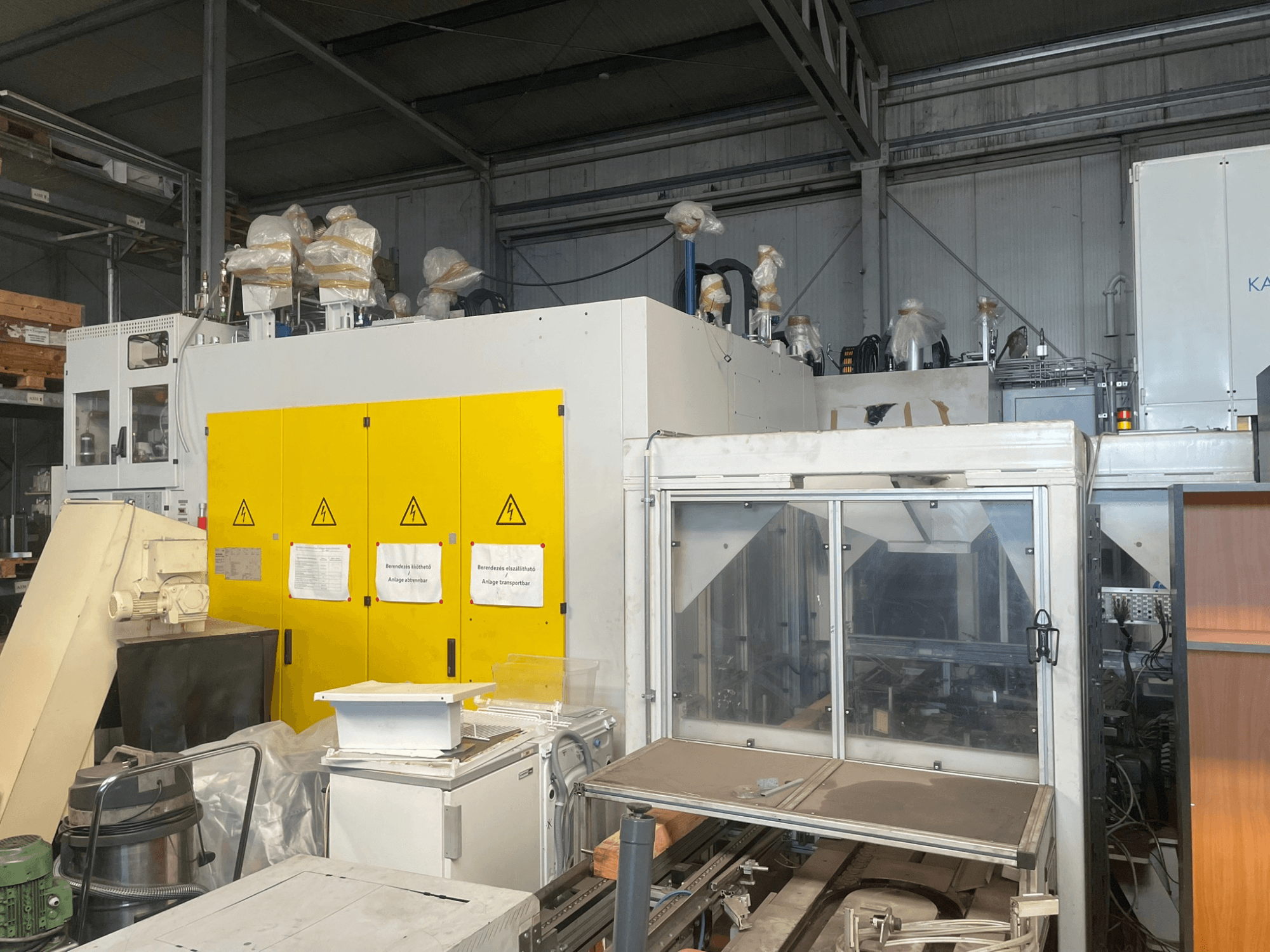 Teollisuuskone, jossa on keltainen ohjauspaneeli, sivukuva, jossa on varoitustarroja ja muovipäällysteet, varastossa.