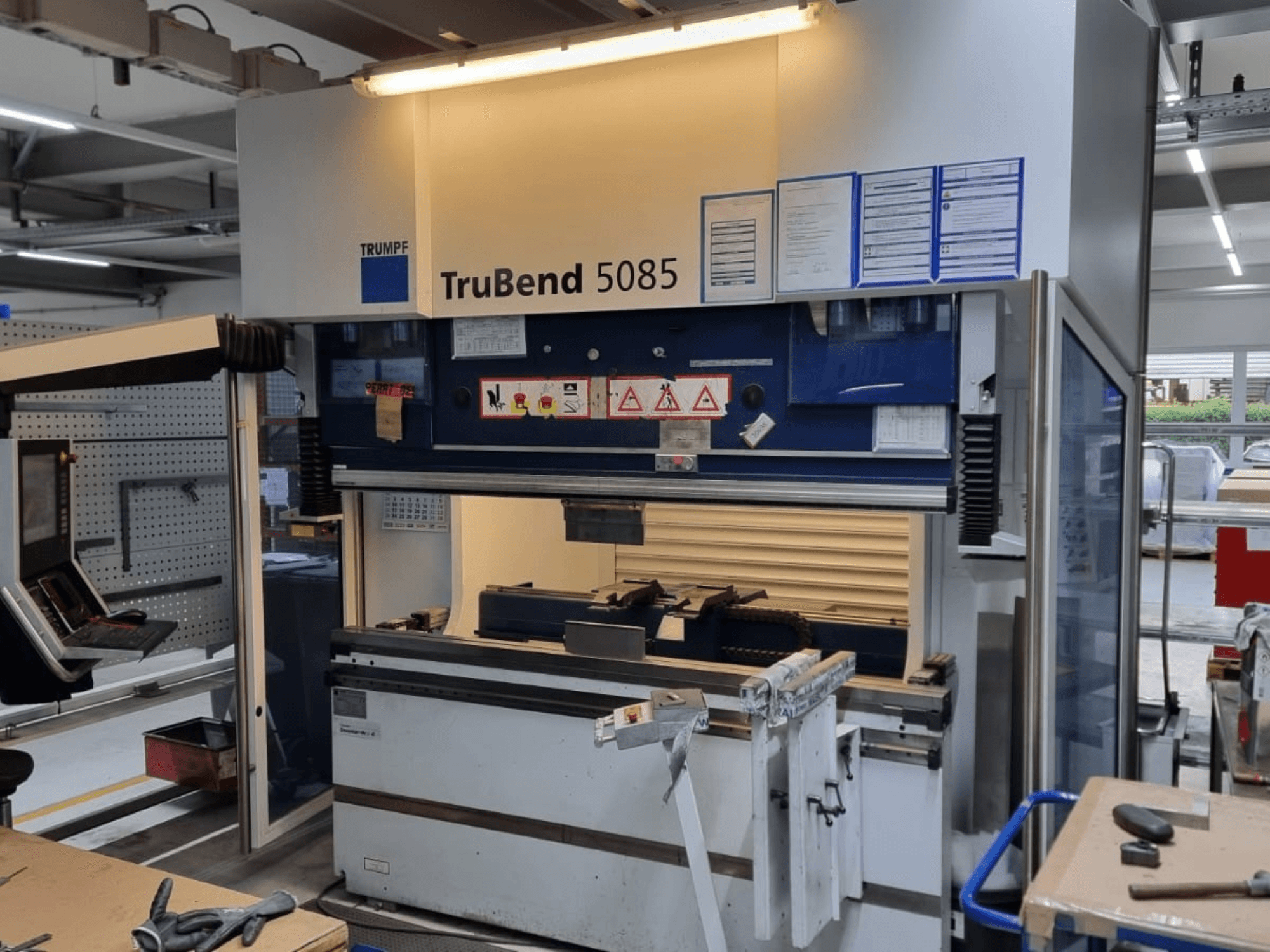TRUMPF TruBend 5085 -taivutuskone, etukuva, jossa näkyy ohjauspaneeli, käyttöpaikka ja turvavaroitukset työpajassa.