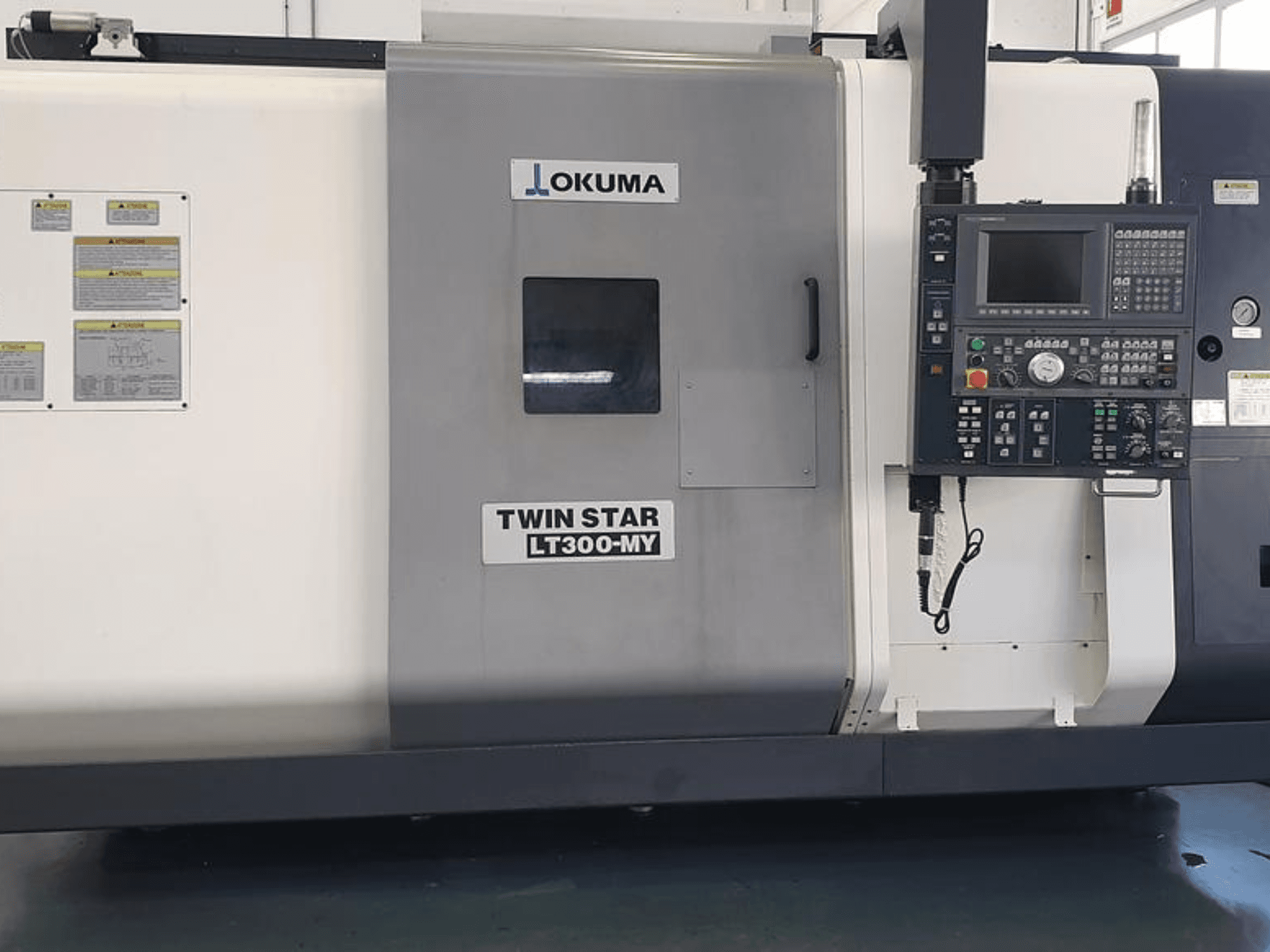 Okuma Twin Star LT300-MY CNC-sorvi sivukuvassa, jossa on ohjauspaneeli, käyttöpainikkeet ja turvatarrat.