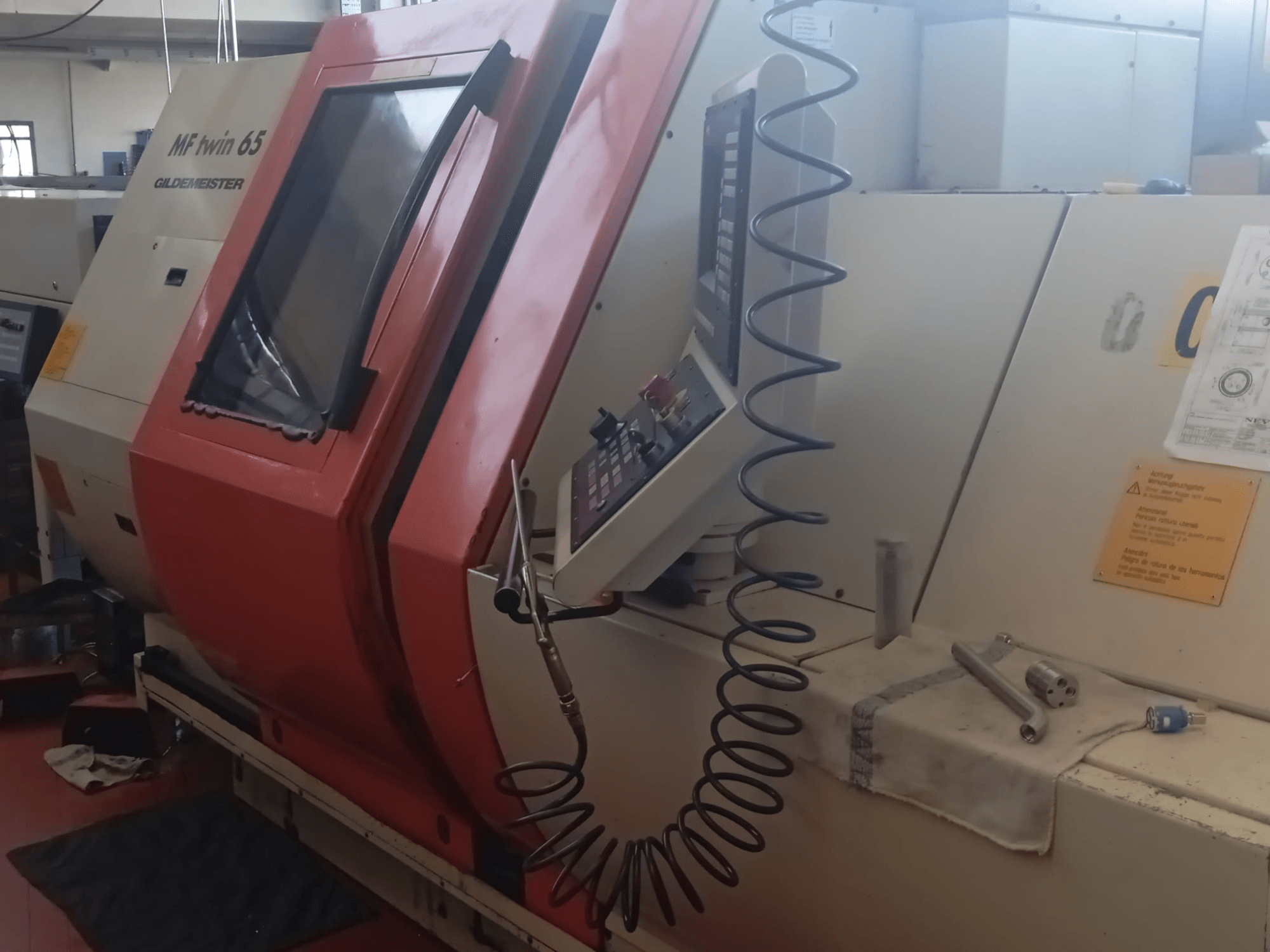 Oranssi-valkoinen MF twin 65 Gliedemeister -kone, etukuva, jossa on ohjauspaneeli ja työkaluja kankaalla.