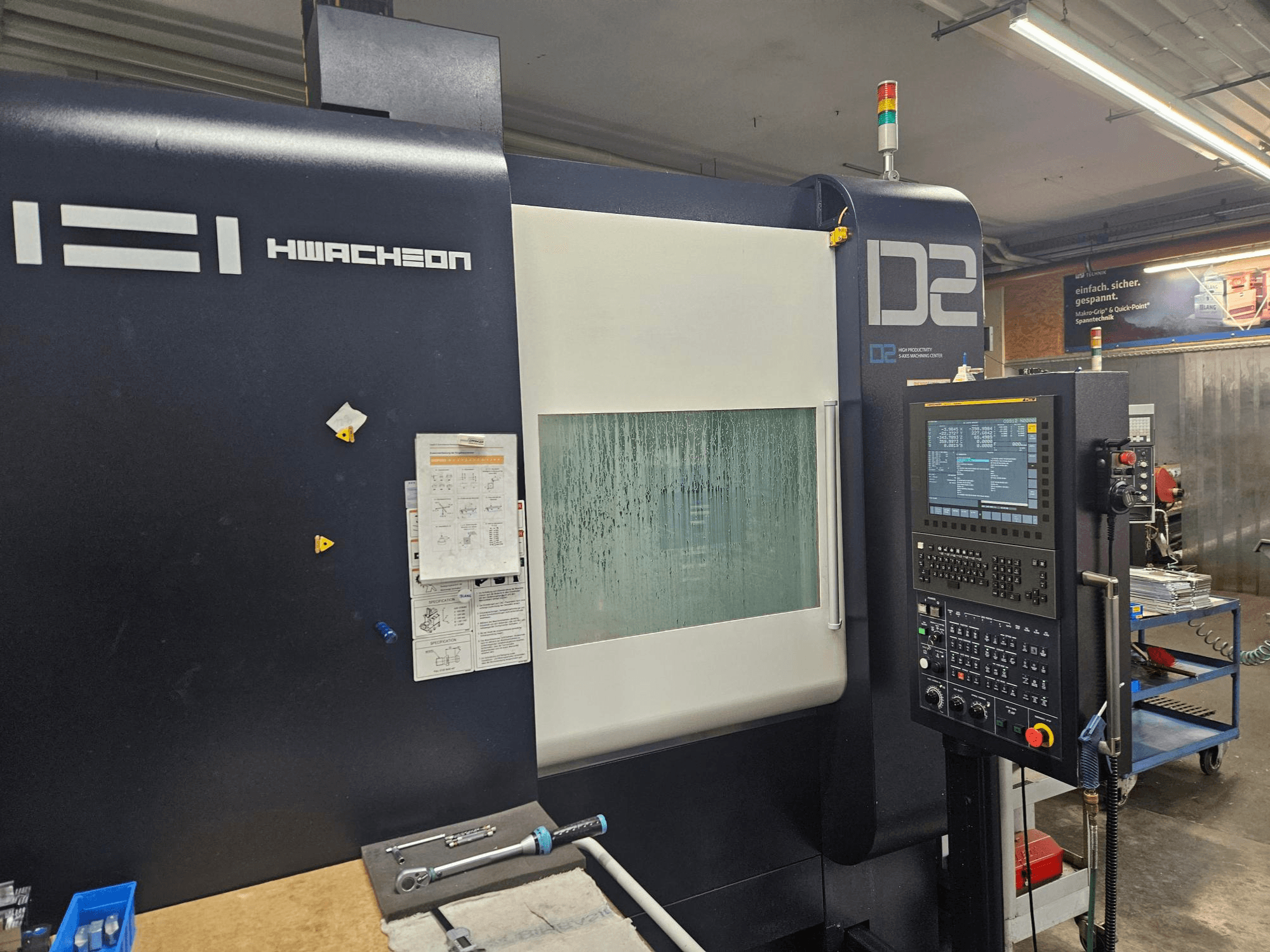 HWACHEON D2-5AX 12k -pystykoneistuskeskus, etunäkymä, jossa näkyy ohjauspaneeli ja sumuinen katseluikkuna.