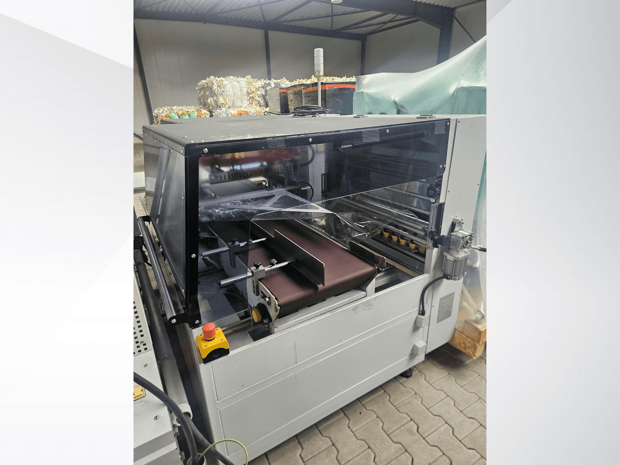 AMTEC Speed Shrink 40 PRO -kone, etunäkymä, jossa näkyy muovinjalostusmekanismi, jossa on läpinäkyvä suojakansi ja kuljetushihna.