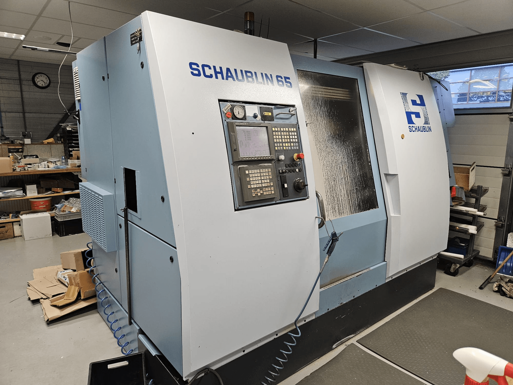 SCHAUBLIN 65 CNC-kone, sivukuva, jossa on ohjauspaneeli, sininen ja harmaa kotelo sekä näkyvä jäähdytysjärjestelmä.