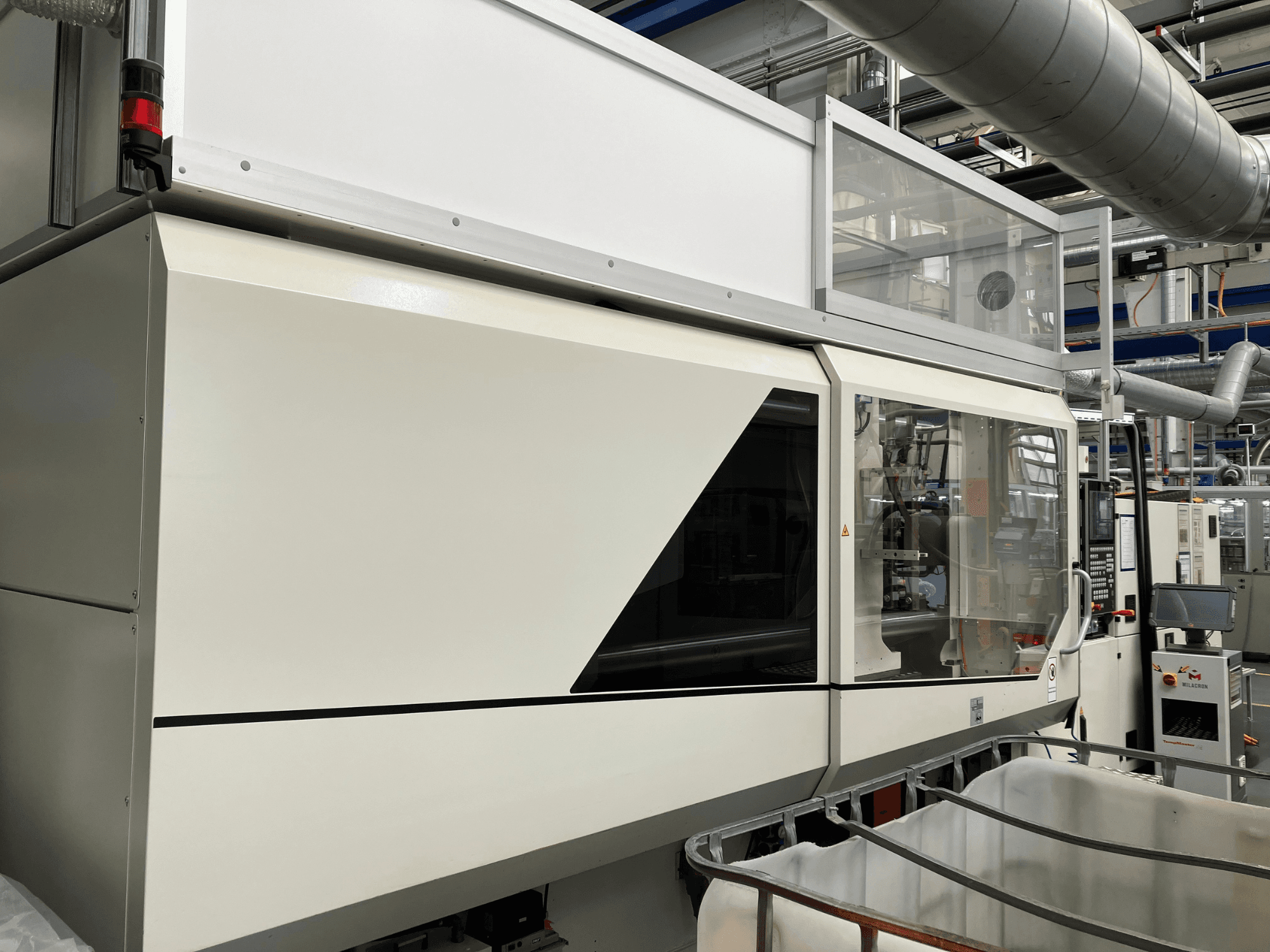 Teollisuuskoneen etunäkymä, jossa on tyylikäs valkoinen muotoilu, näyttöpaneeli ja lasiosa komponenttien näkyvyyttä varten.