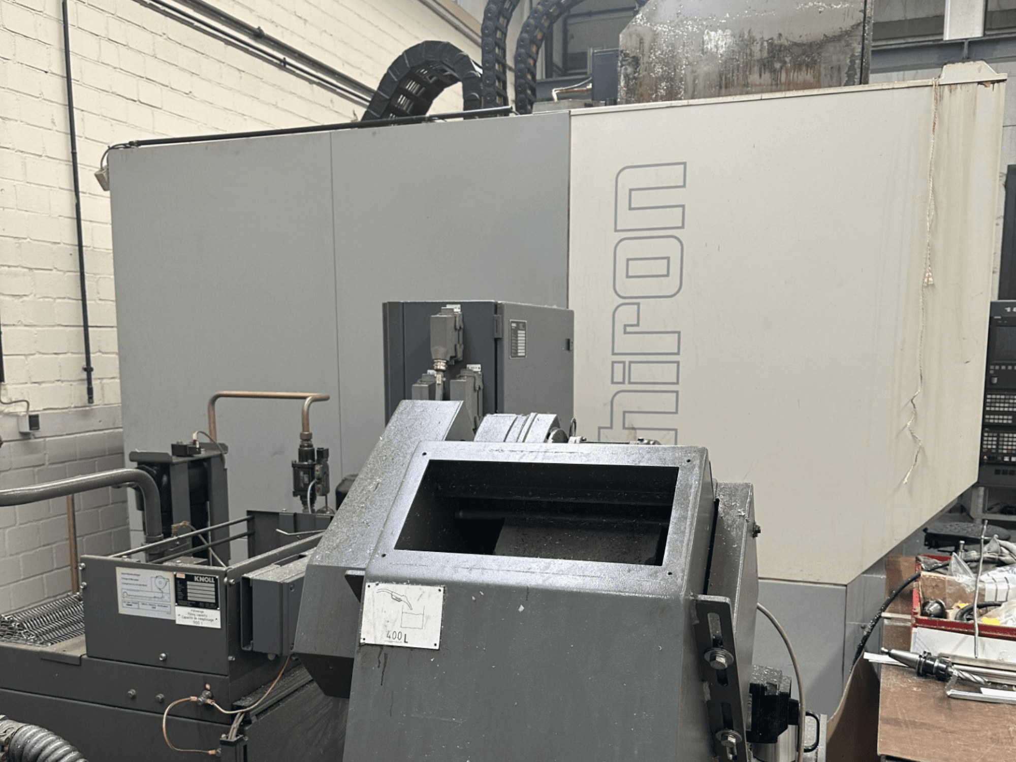 BRAND: Chiron; Etukuva teollisesta CNC-koneesta, jossa on harmaa ulkokuori, ohjauspaneeli näkyvissä ja koneen osat tarkennettuna.