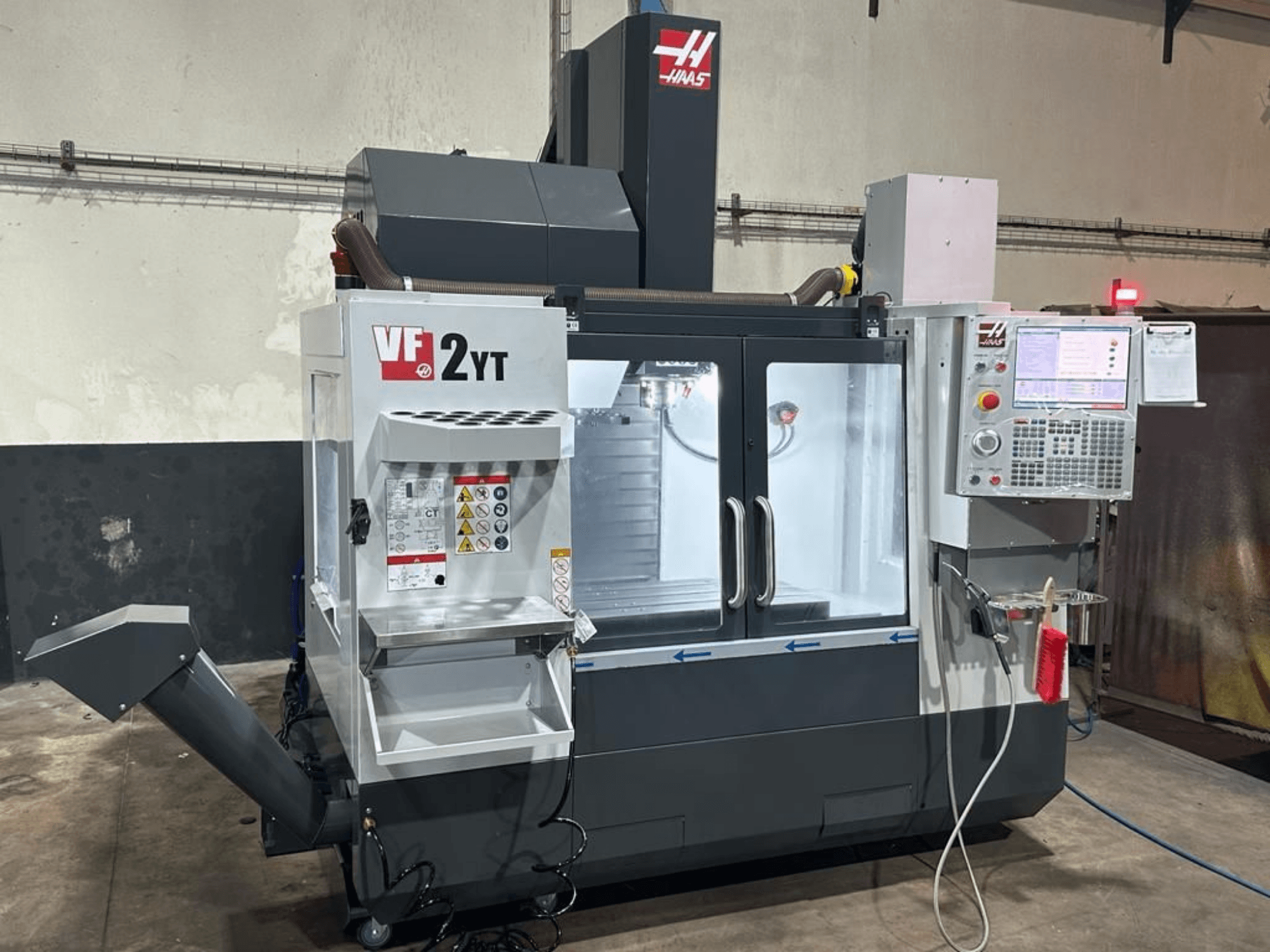 HAAS VF-2YT-EU -pystykoneistuskeskus edestä katsottuna; kuvassa näkyvät ohjauspaneeli ja työkalujen säilytyslokero.