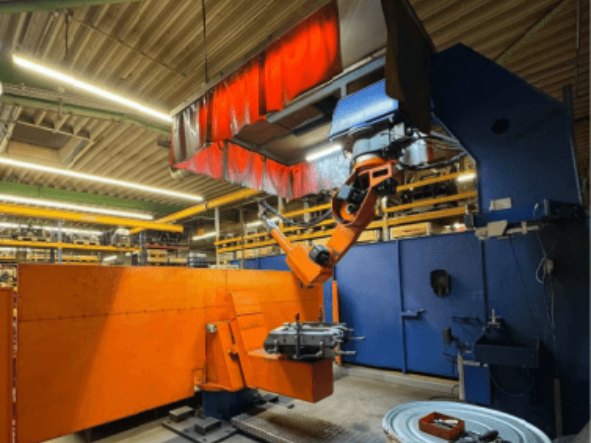 CLOOS Romat 350 e -hitsausrobotti teollisuusympäristössä, etukuva oranssilla käsivarrella, joka pitää työkappaletta yläverhon alla.