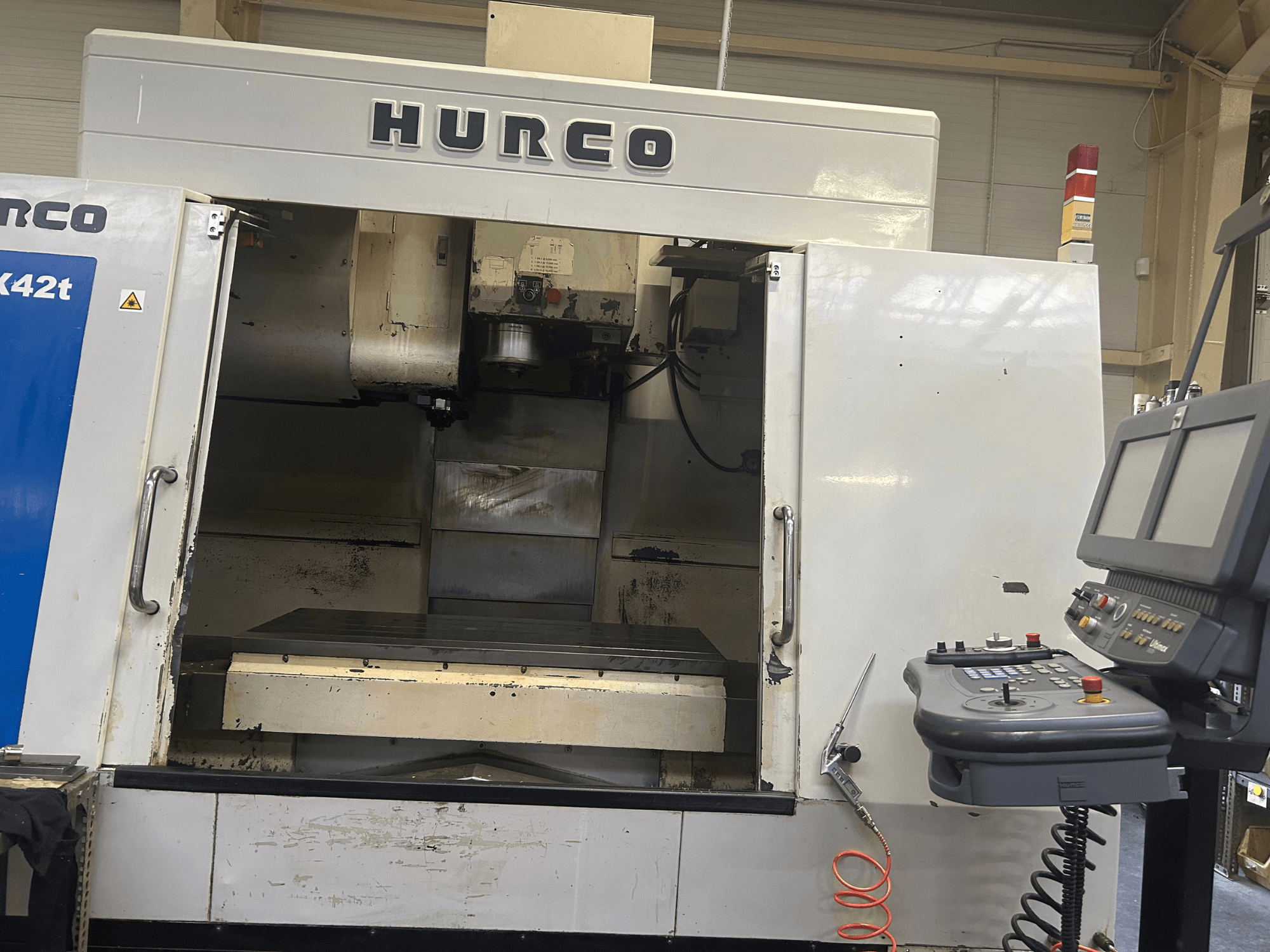 Hurco VMX42T CNC-jyrsinkone etukuvassa, jossa on avoin työtila ja ohjauspaneeli, jossa on painikkeet ja näyttö.