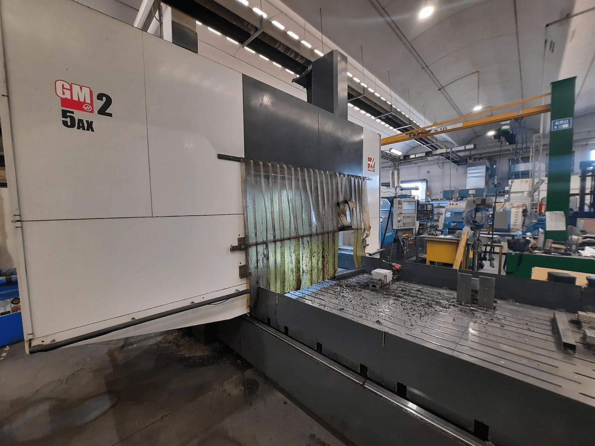 GM 2 5AX CNC-kone työpajassa, sivukuva, jossa näkyy työskentelyalue ja metallilastut sängyn pinnalla.