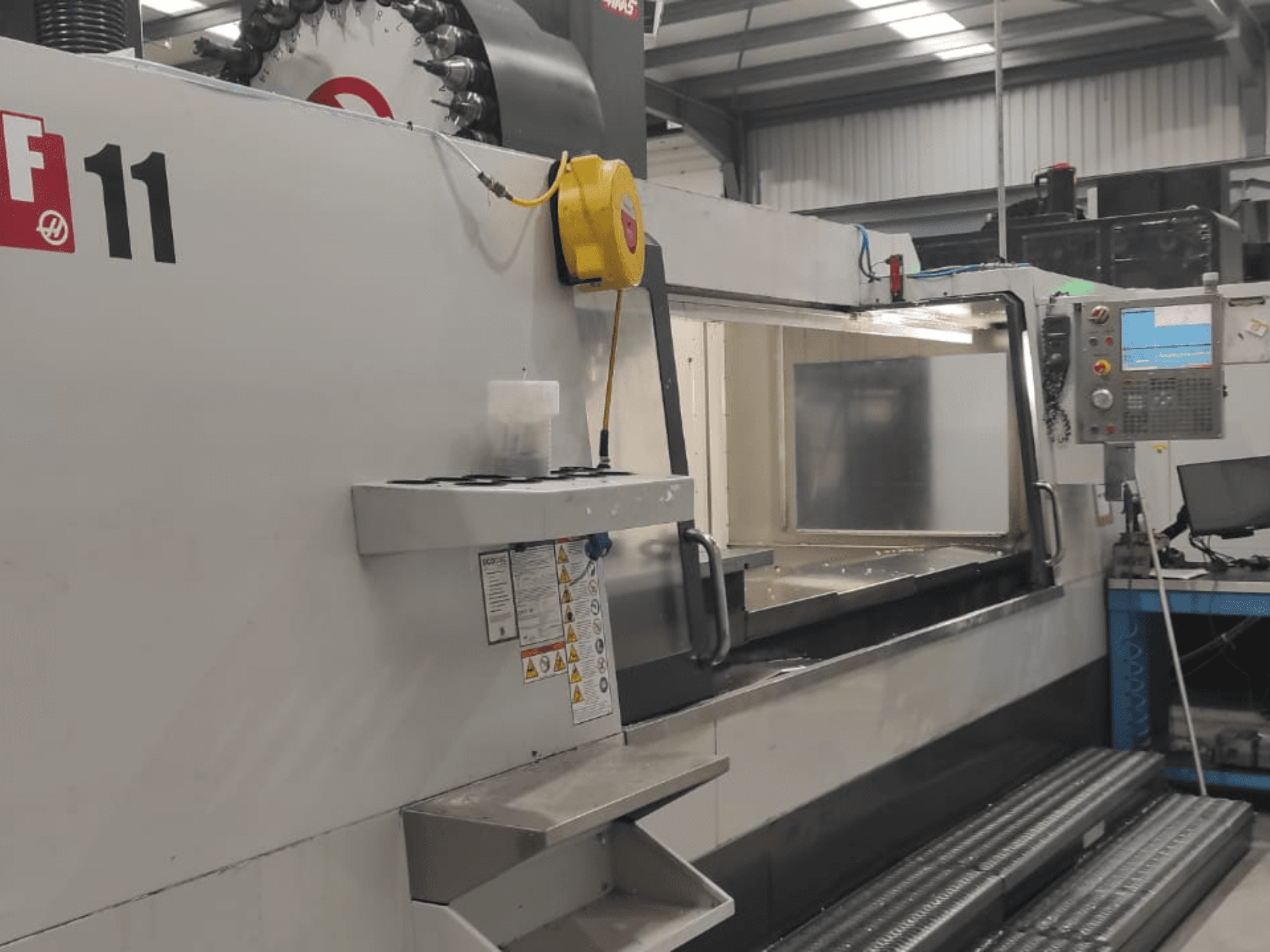 Haasin kone, malli VF-11, kuvattuna edestäpäin, kun ohjauspaneeli, suuri työskentelyalue ja turvatarrat ovat näkyvissä.