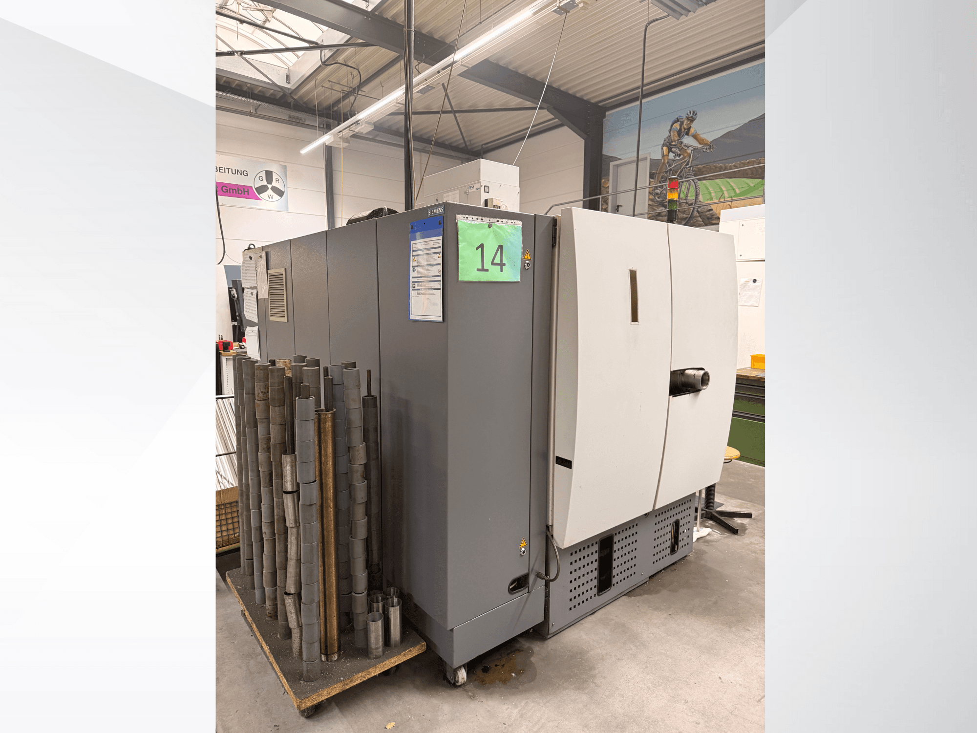 Siemensin harmaa teollisuuskone sivukuvassa, vieressä lieriömäisiä metallikappaleita ja näkyvissä laitetarroja.