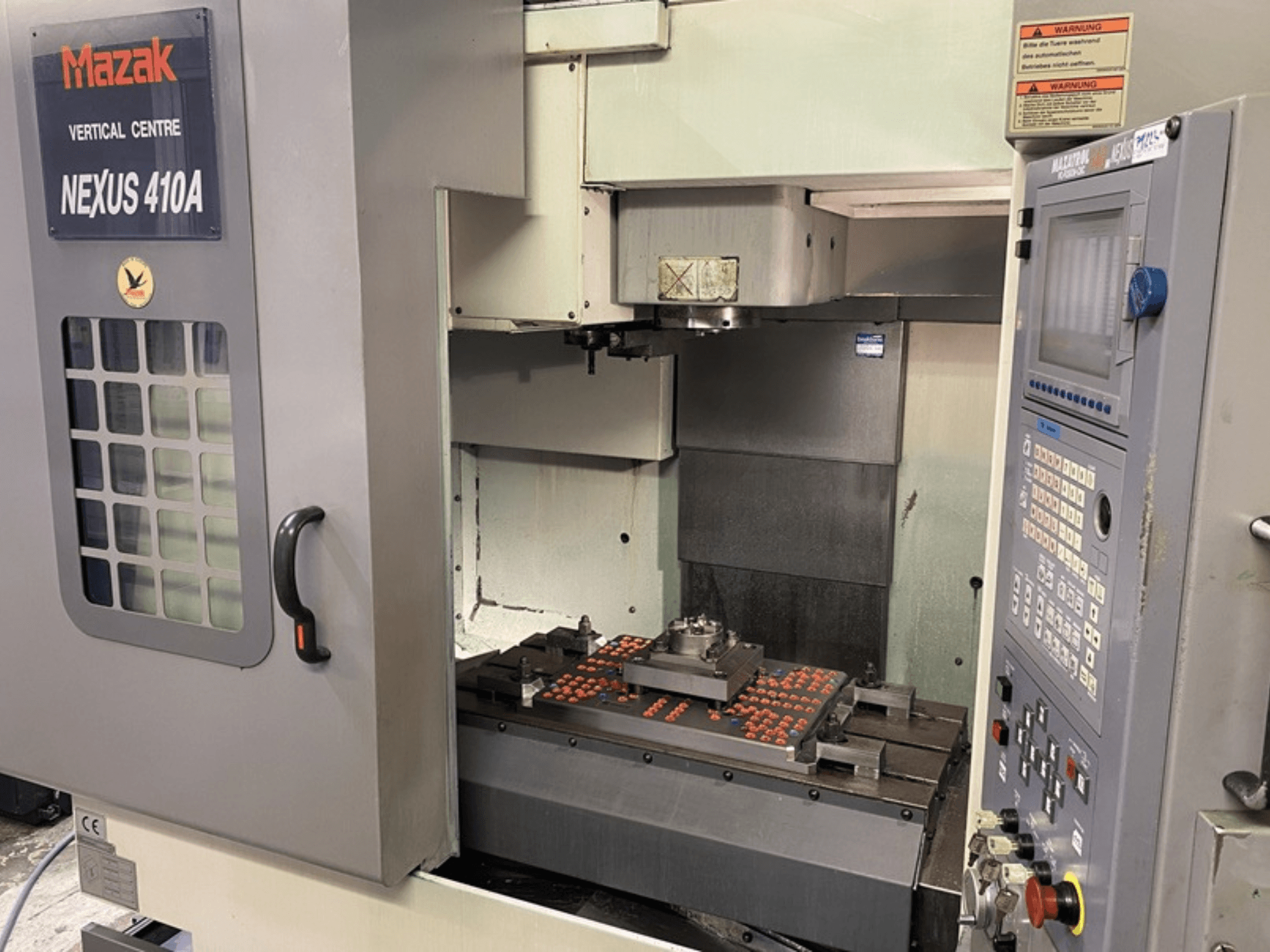 Mazak VCN410 -pystytyöstökeskus, etukuva, jossa näkyy ohjauspaneeli ja koneen sisätilat, kun työkappale on asennettu.