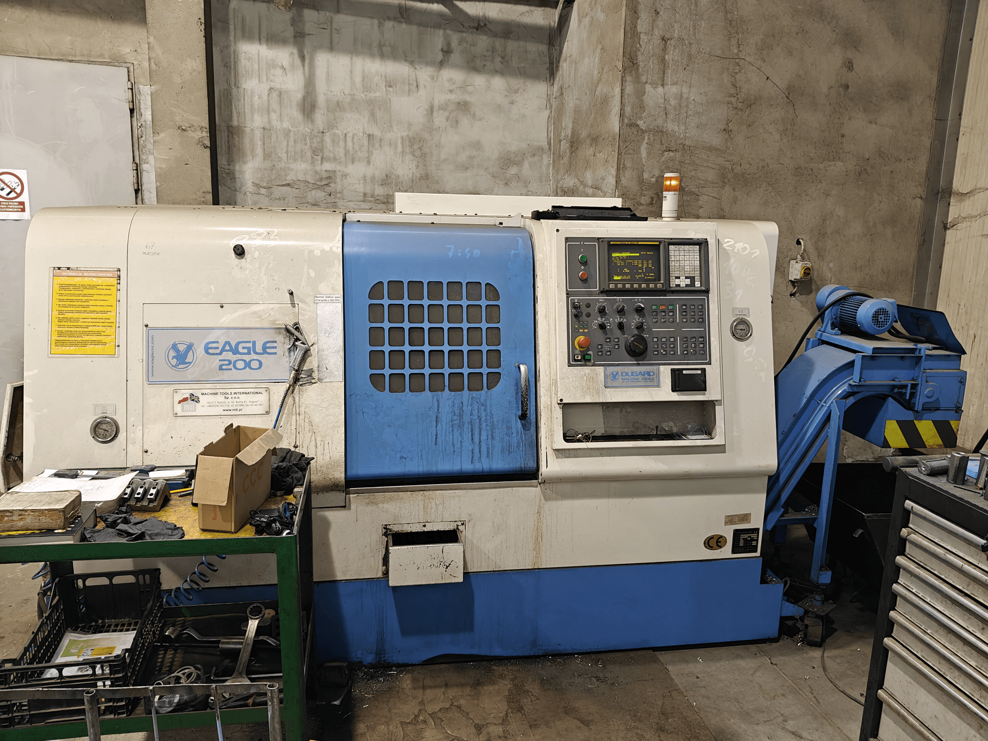 Eagle 200 CNC-kone, etukuva, jossa ohjauspaneeli, erilaisia työkaluja vihreällä kärryllä. Näkyvää kulumista ja toimintavalot.