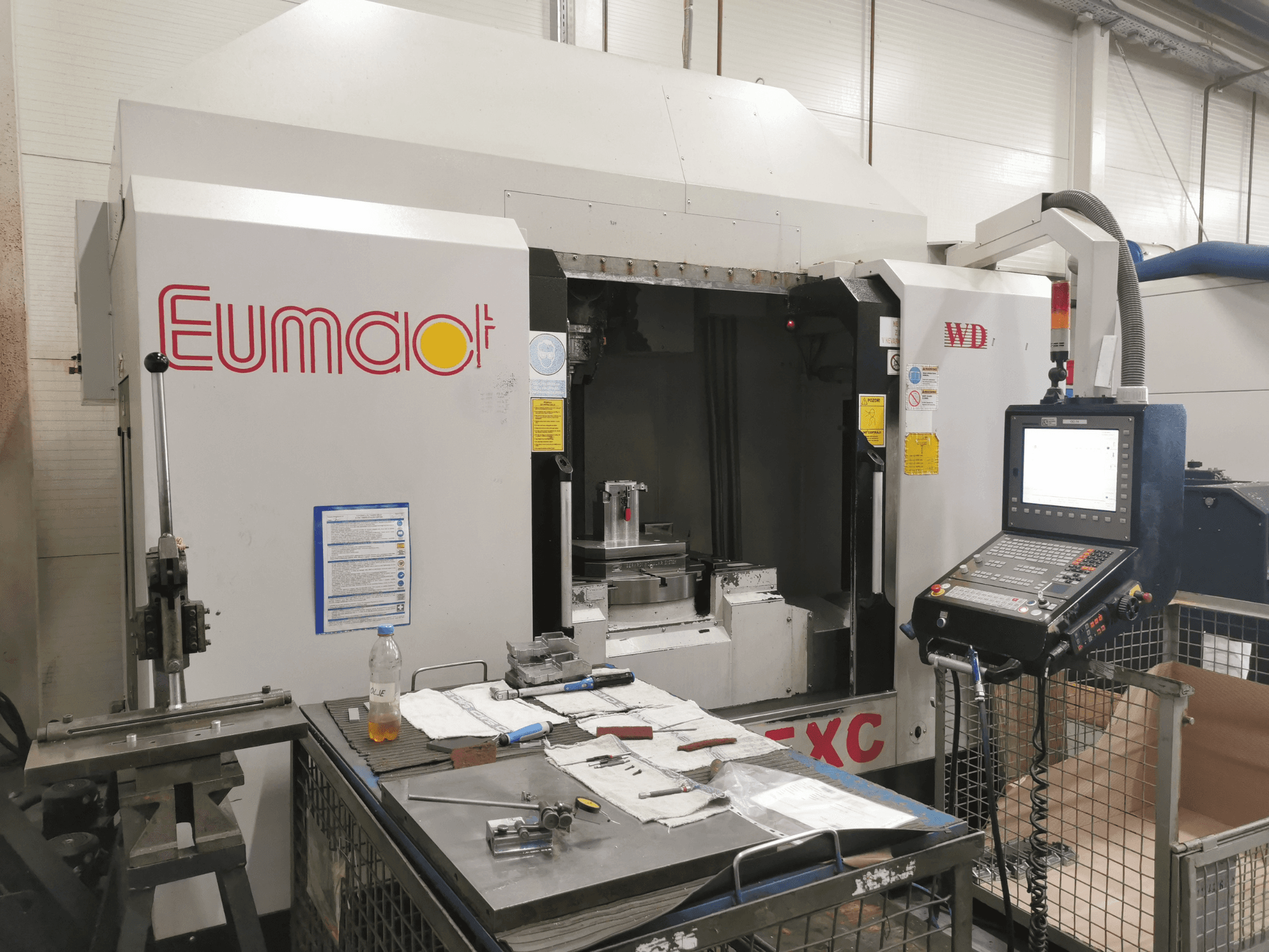 Etukuva Eumdaot CNC-koneesta, jossa on ohjauspaneeli, työkaluja ja työpinta täynnä komponentteja ja materiaaleja.