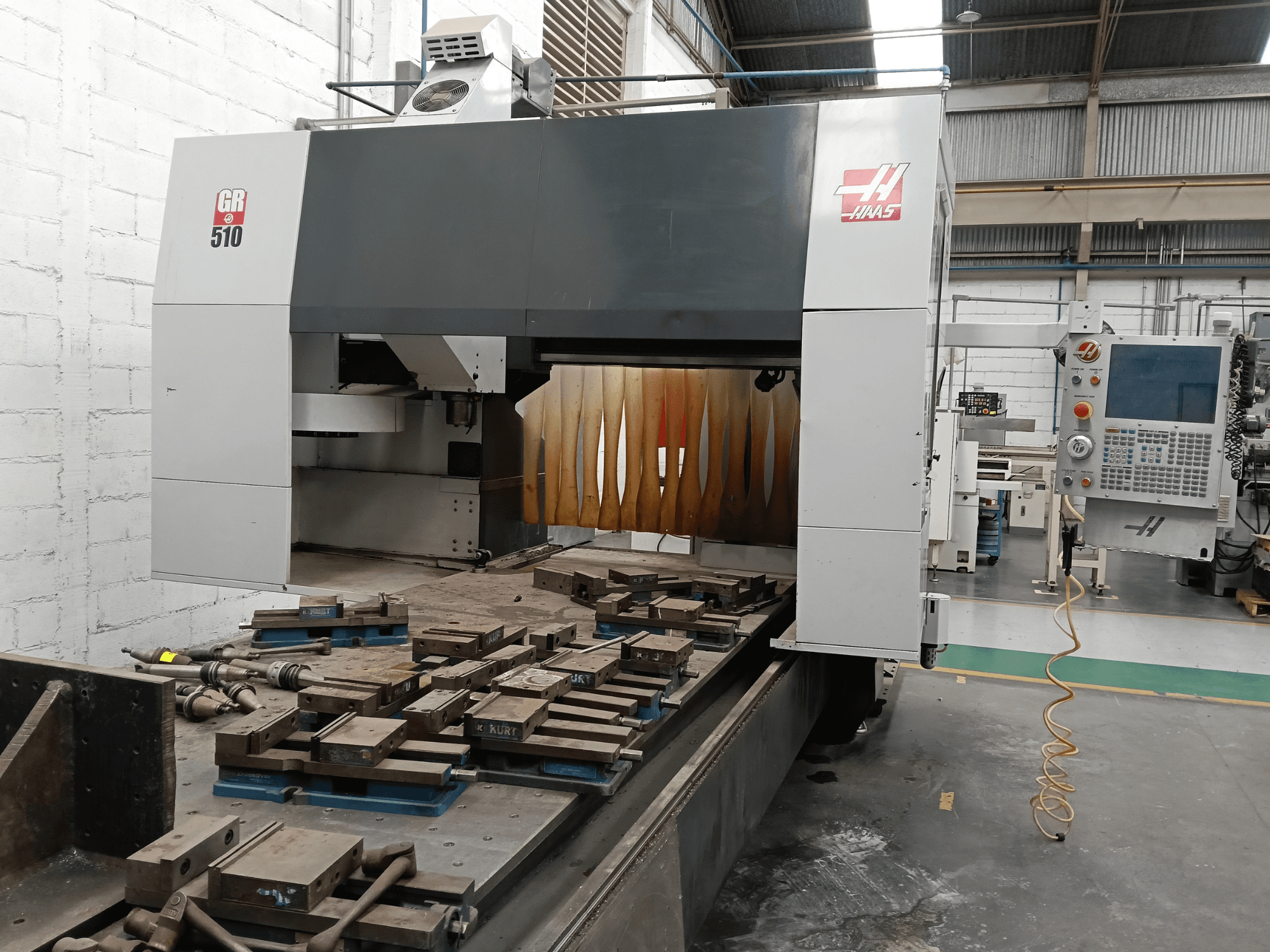 HAAS GR-510 -portaalijyrsinkoneen etunäkymä, jossa näkyvät ohjauspaneeli ja työpöydällä olevat työstetyt työkappaleet.
