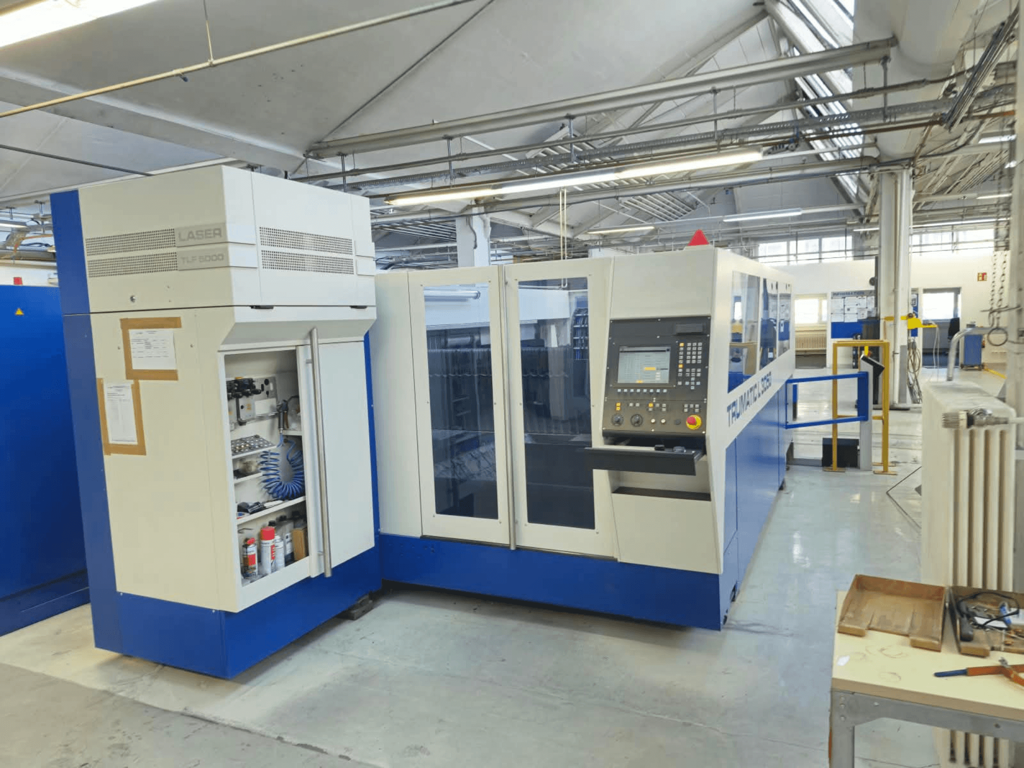 TRUMPF TruLaser L3050 CO₂-laserleikkauskone, etunäkymä, jossa näkyy ohjauspaneeli ja huoltoluukku, tehdasasetuksissa.