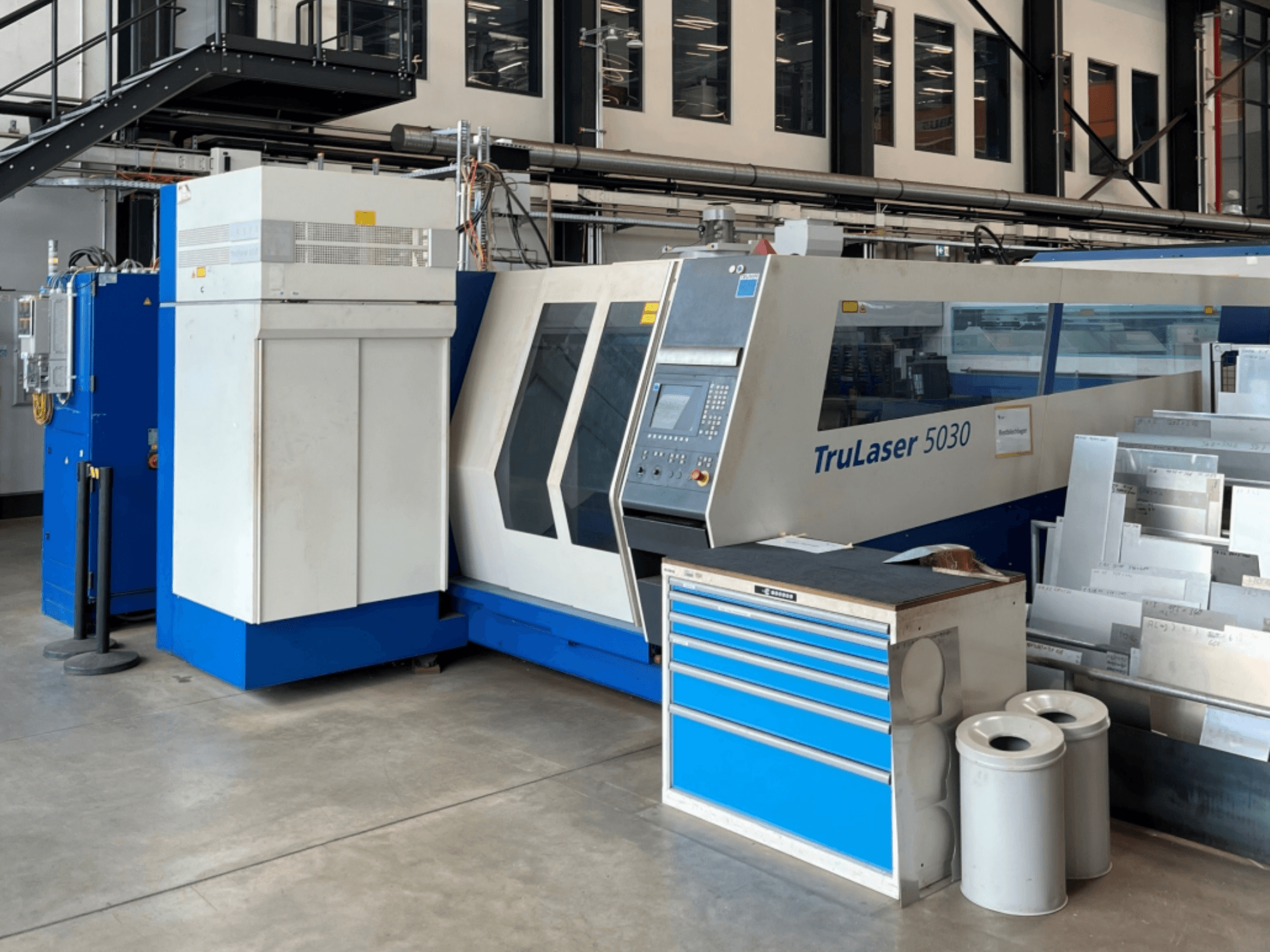 TRUMPF TruLaser 5030 CO₂-laserleikkauskone edestä katsottuna; kuvassa näkyy ohjauspaneeli ja sen vieressä oleva työpöytä, jolla on metallilevyjä.