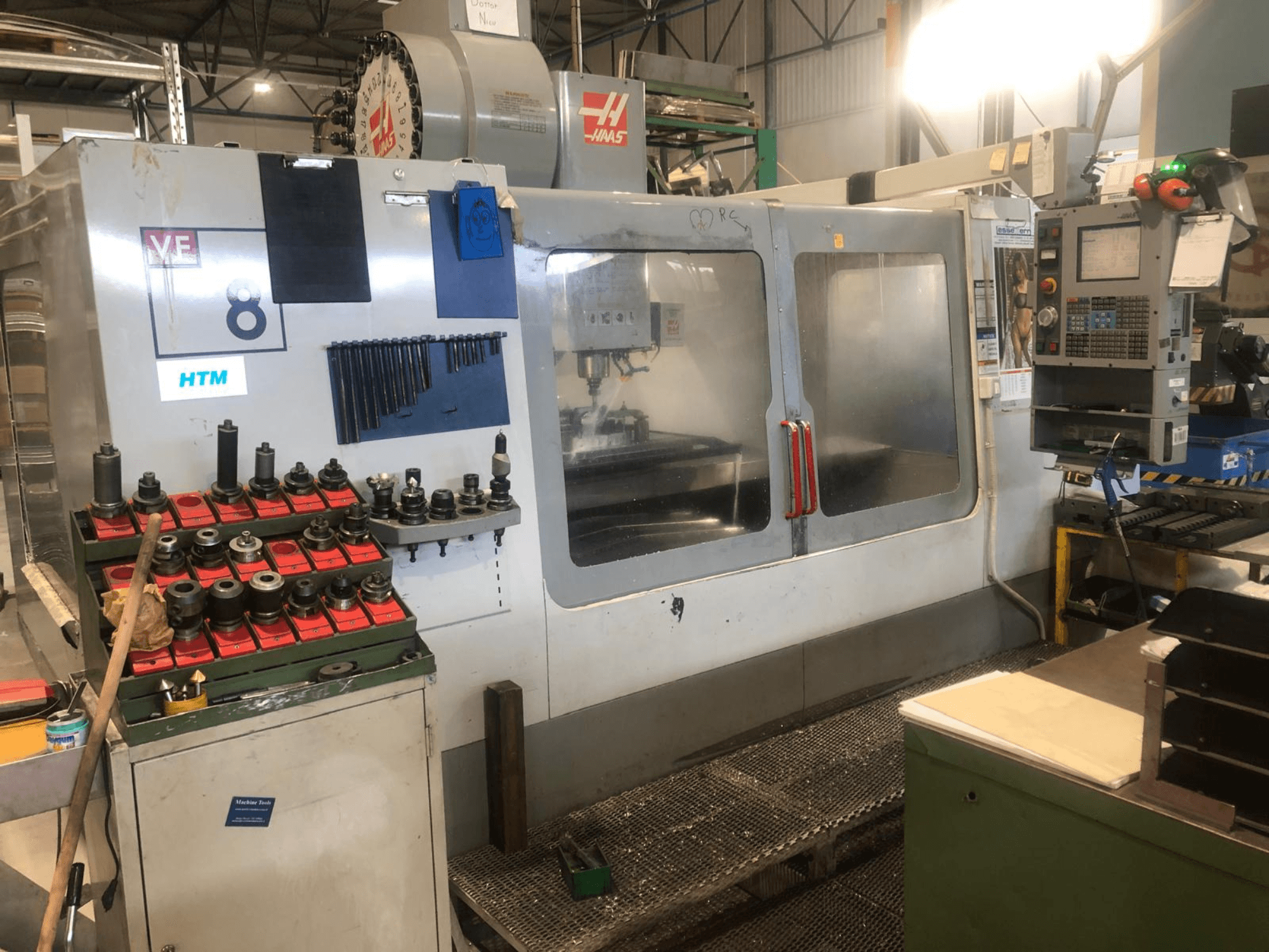 Haas CNC-kone työpajassa, etukuva; työkalut ja hallintalaitteet näkyvissä, mallin yksityiskohdat ja järjestetyt työkalunpitimet.