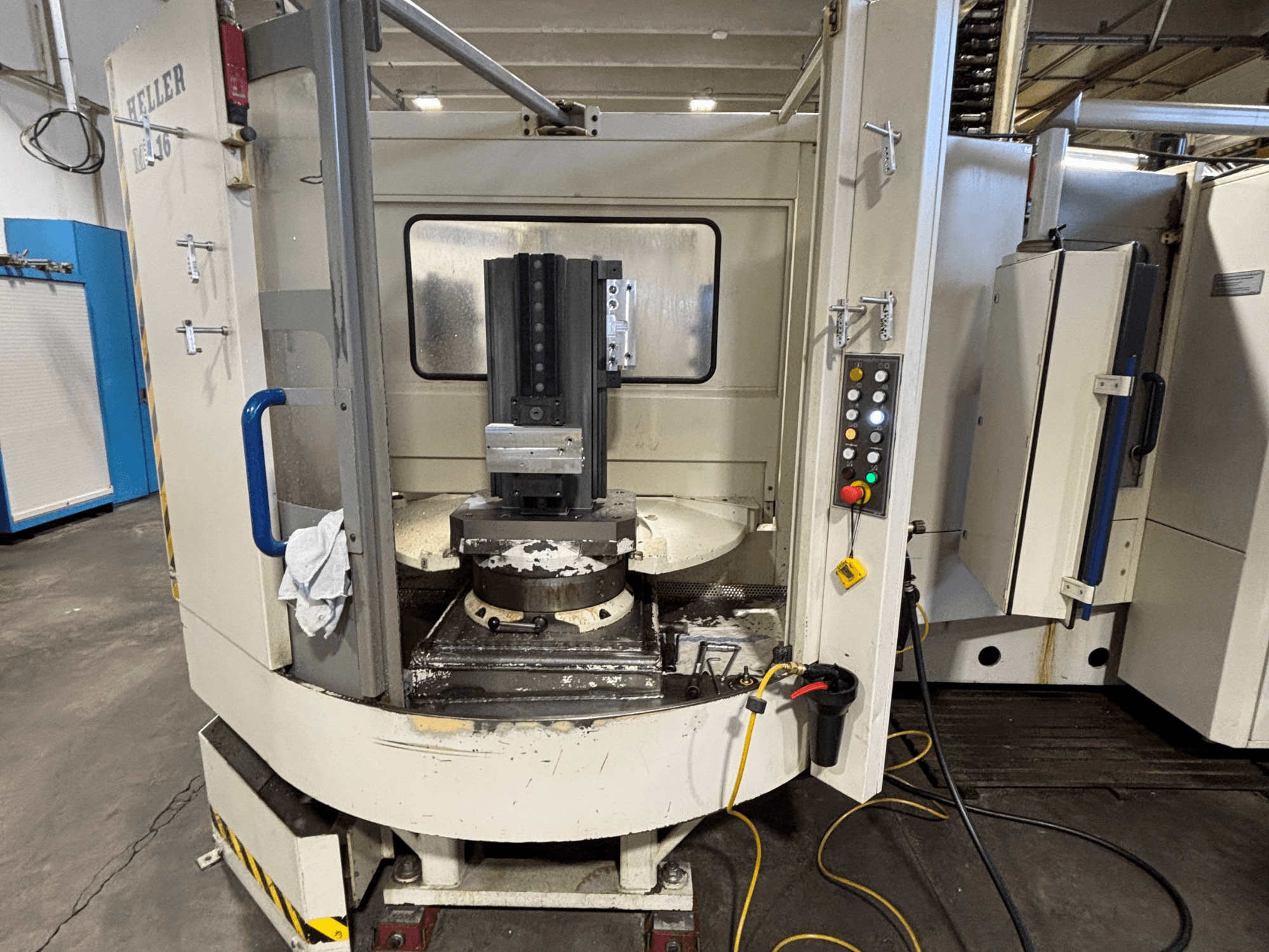 Heller-työstökeskus, malli vertikaalinen, etukuva, jossa näkyy kara, ohjauspaneeli ja työpöytä kiinnitettyine laitteineen.